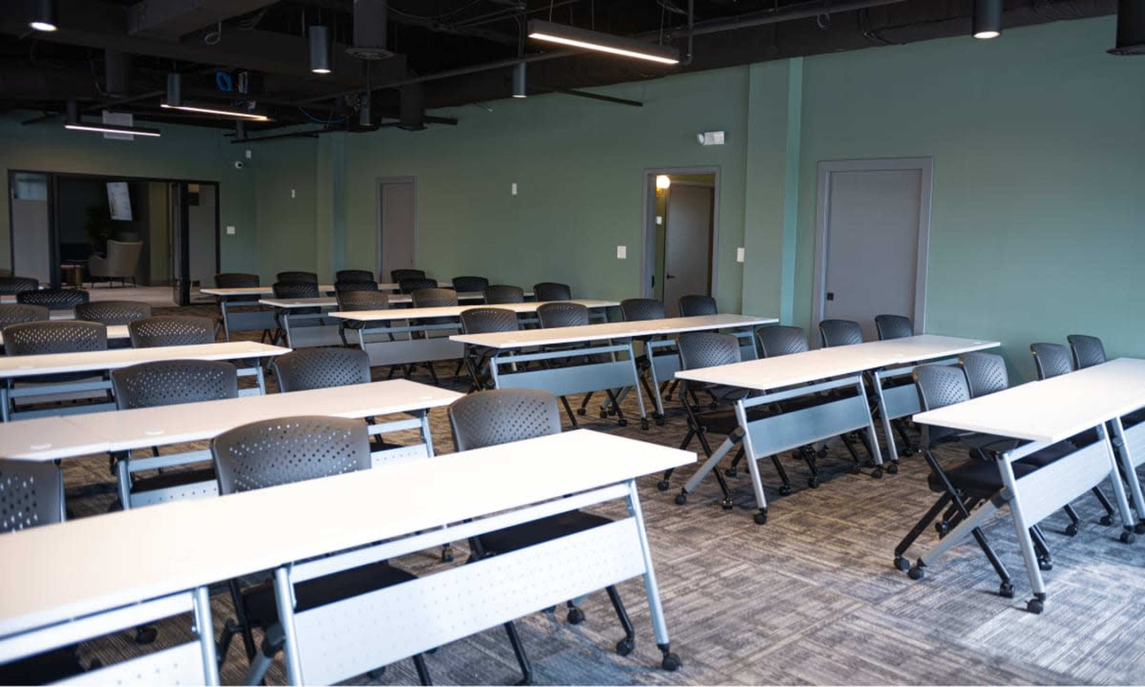A classroom features rows of tables arranged for group work, with black chairs and green walls.