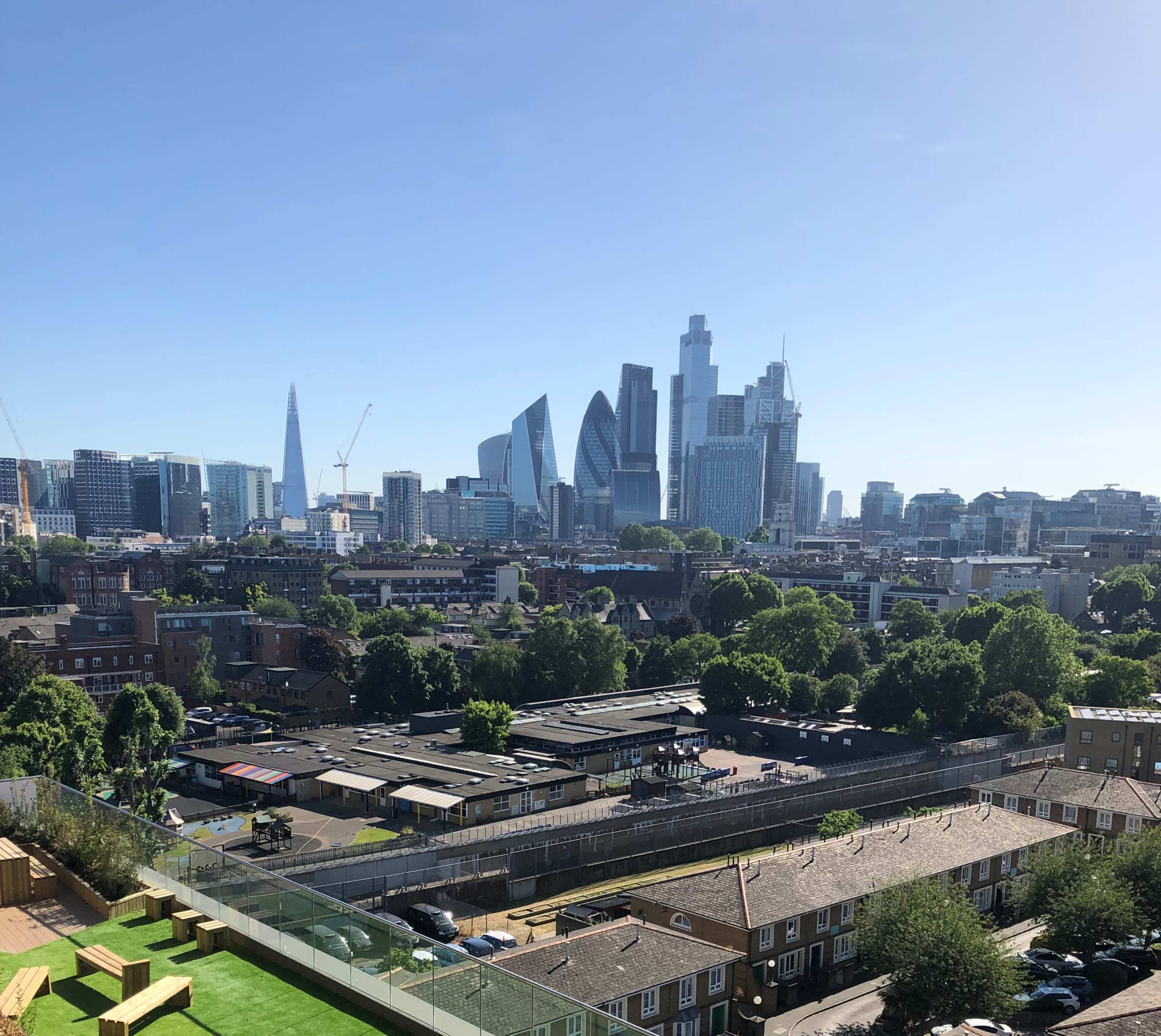 A panoramic view of the London skyline featuring modern skyscrapers, including The Shard, against a clear blue sky.