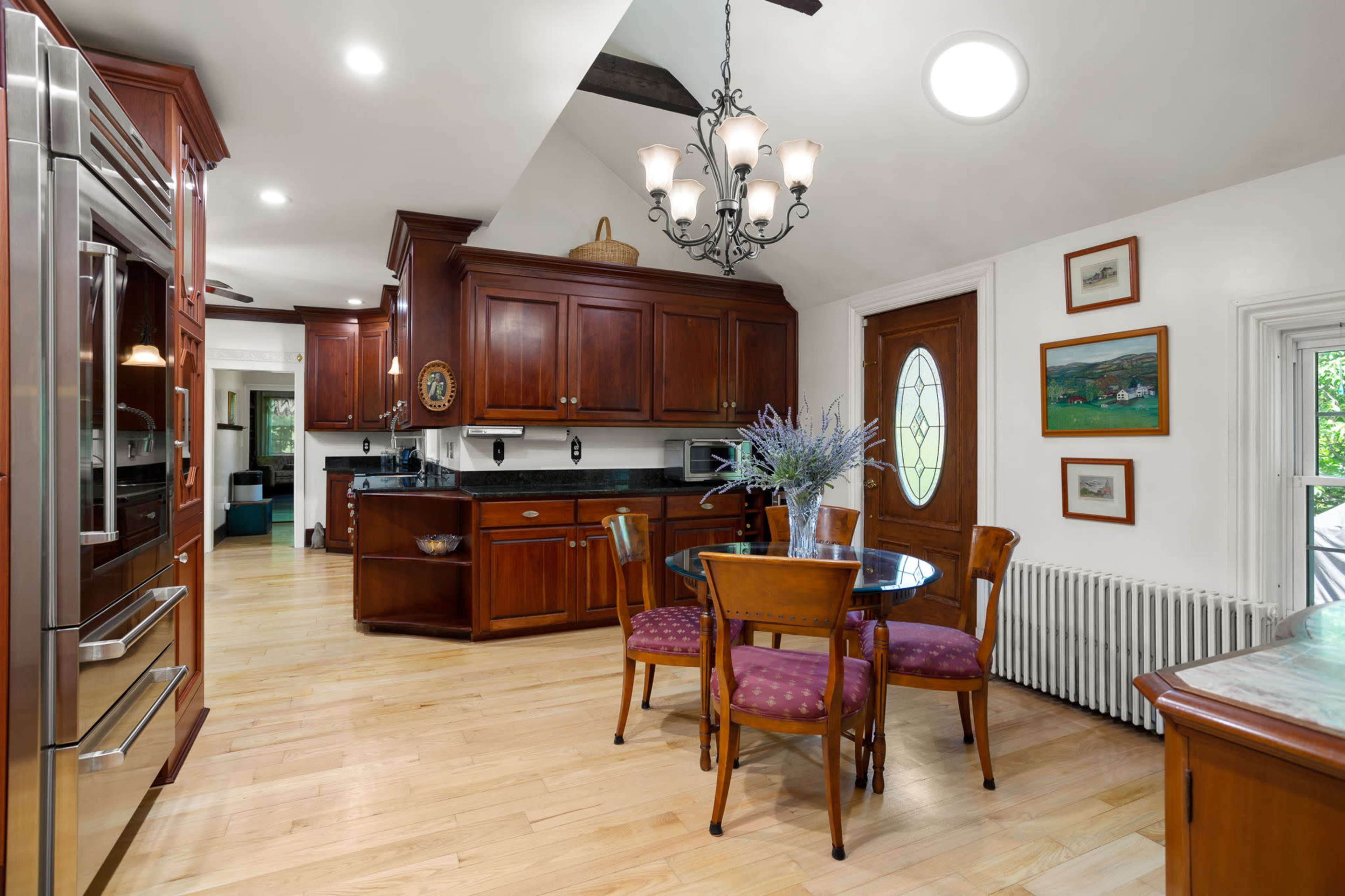 A well-lit kitchen featuring wooden cabinets, a round dining table with upholstered chairs, and stainless steel appliances.