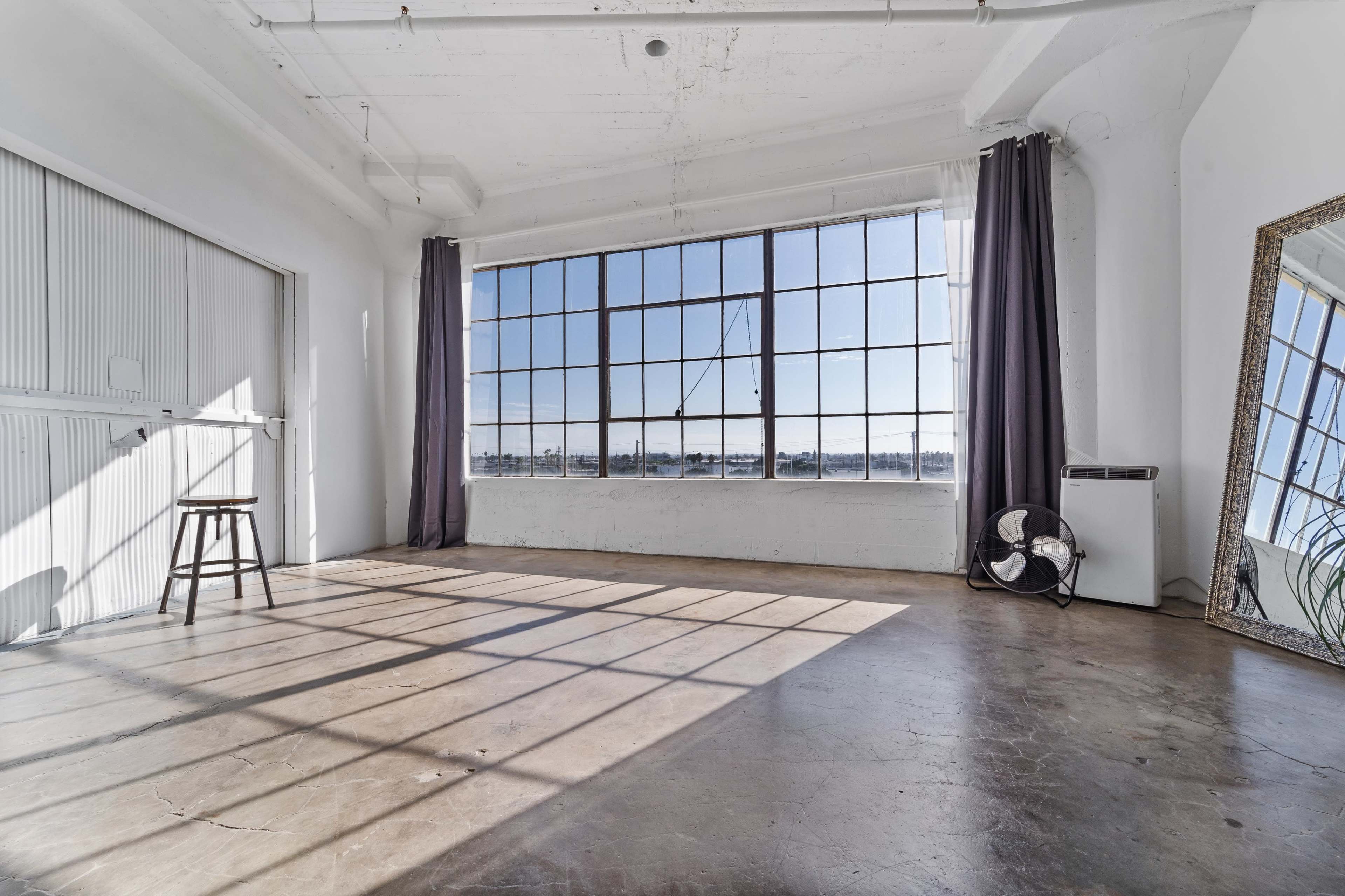 A spacious, empty room features a large window with natural light, casting shadows on the polished concrete floor.