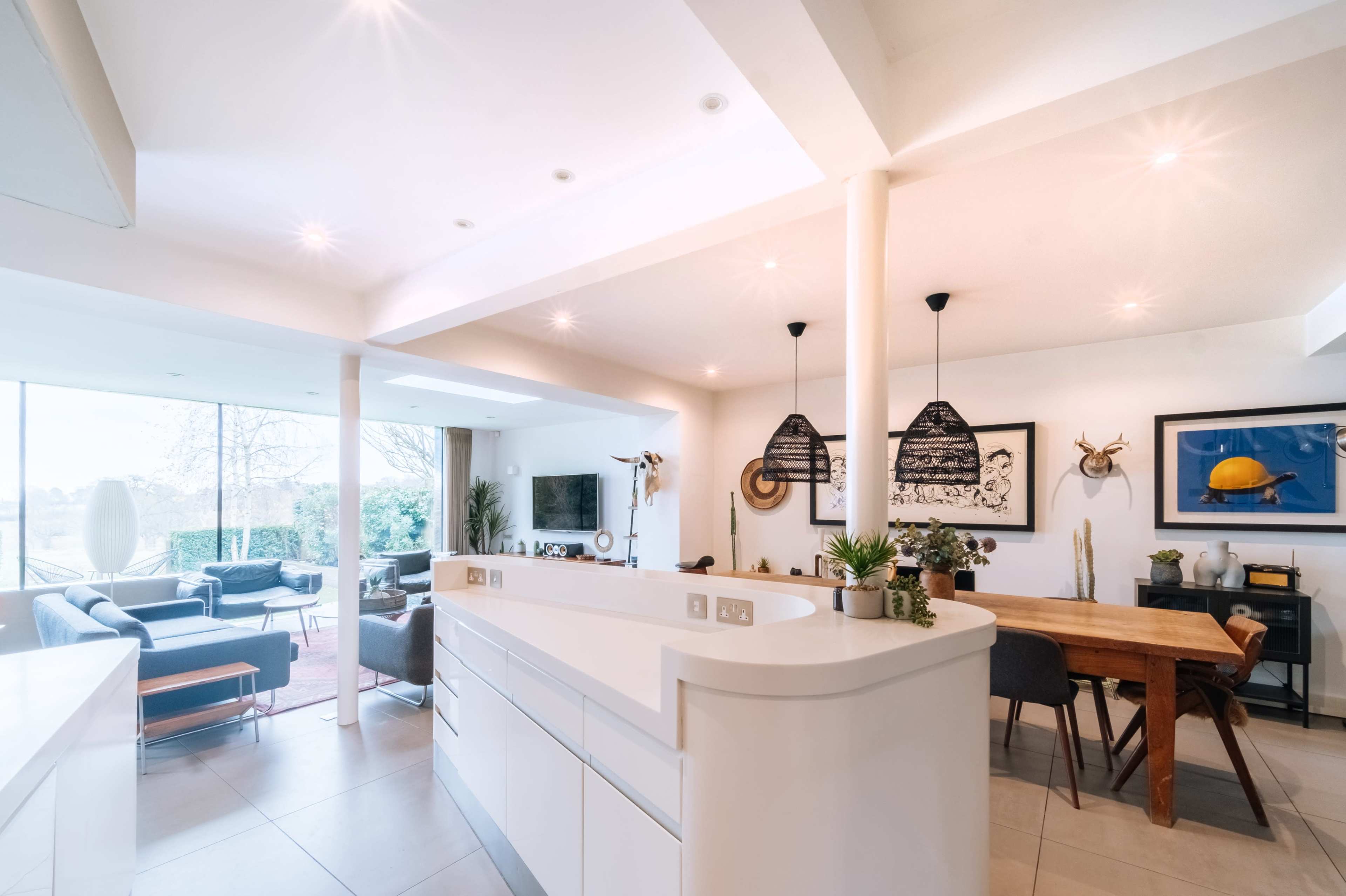 A modern kitchen and dining area with a white countertop, wooden dining table, and large windows that provide natural light.