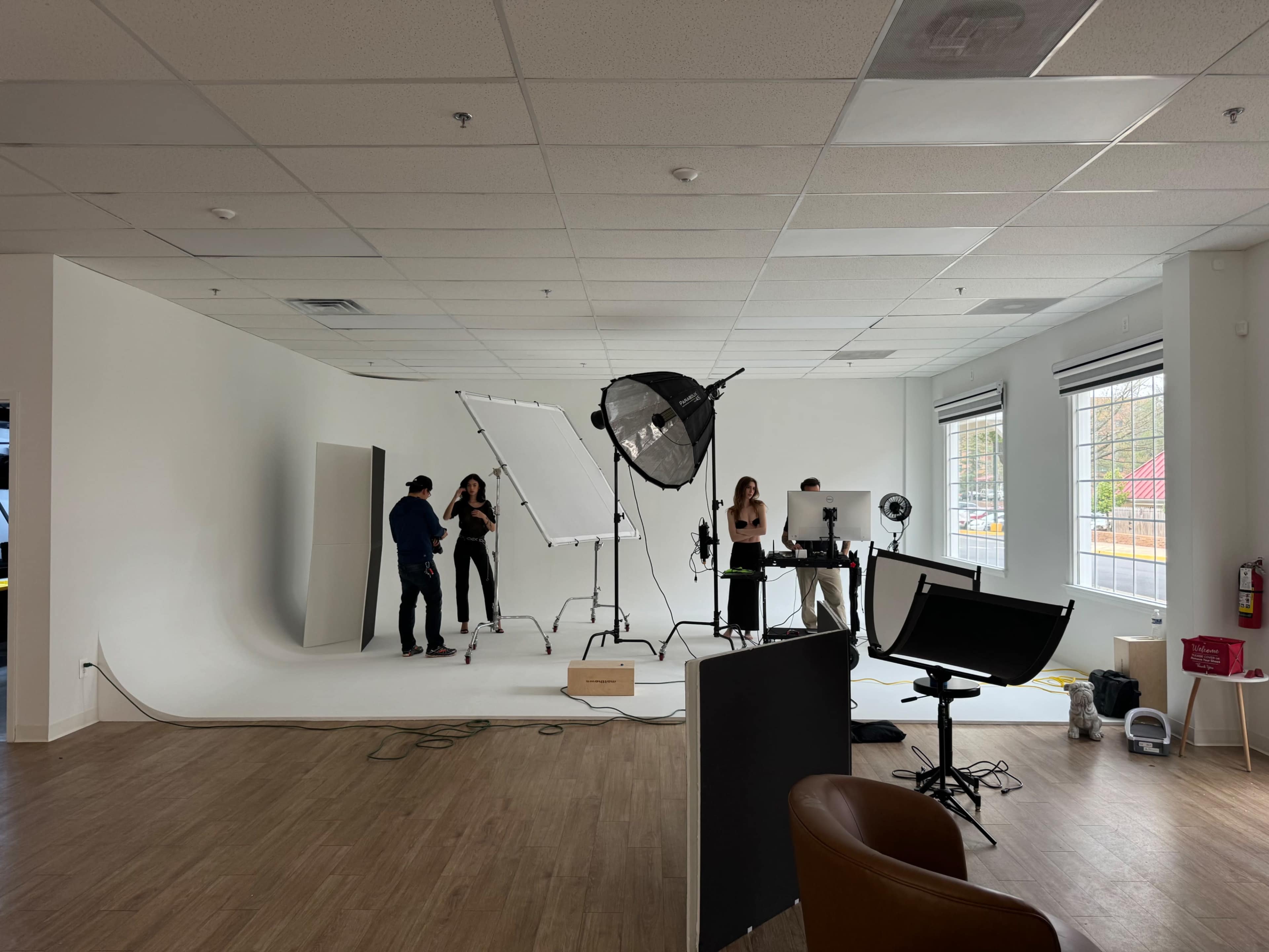 A photography studio setup is seen with a backdrop, lighting equipment, and several people preparing for a photoshoot.