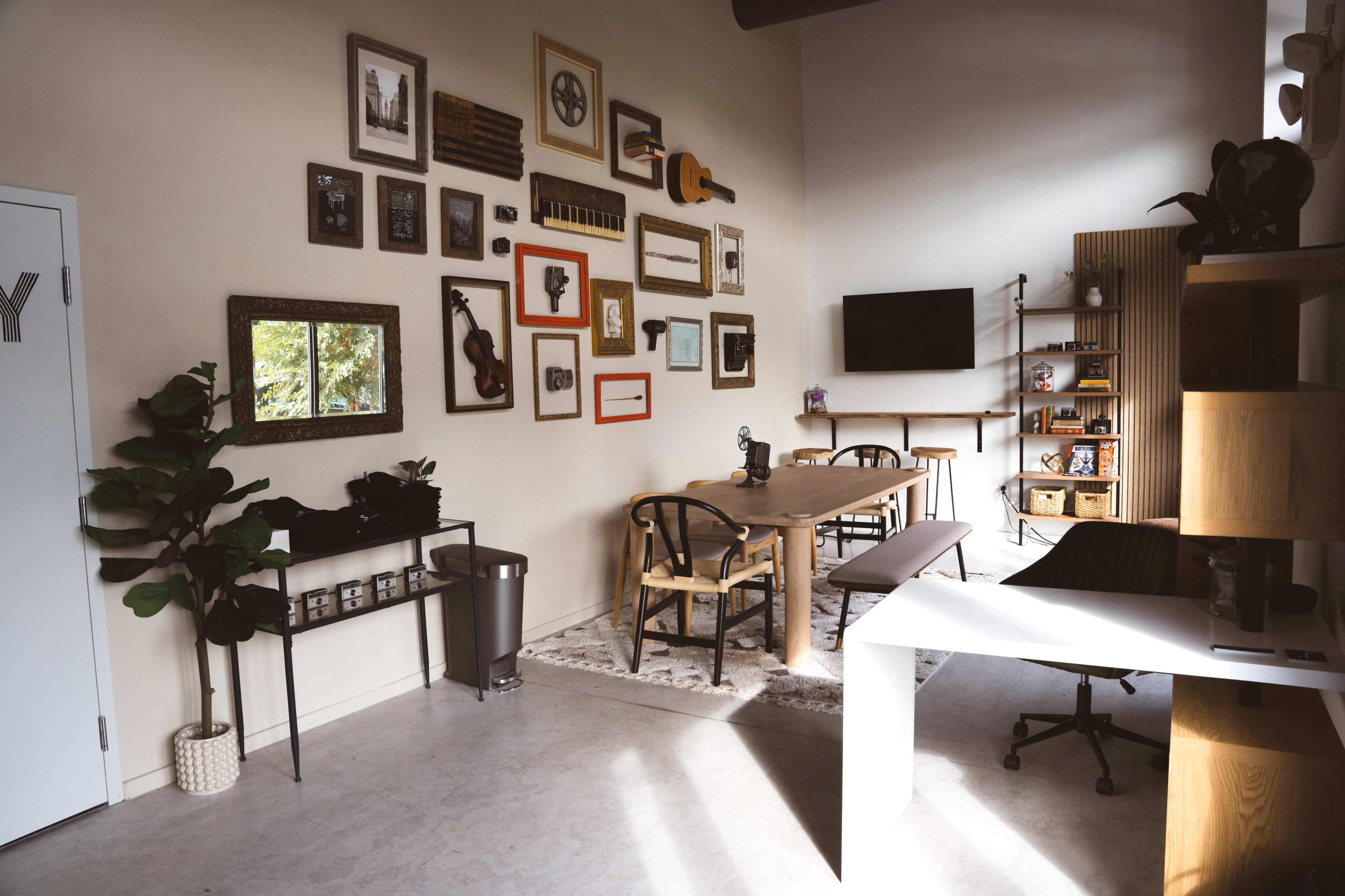 A modern workspace featuring a wooden table surrounded by chairs, adorned with framed artwork and a television on the wall.