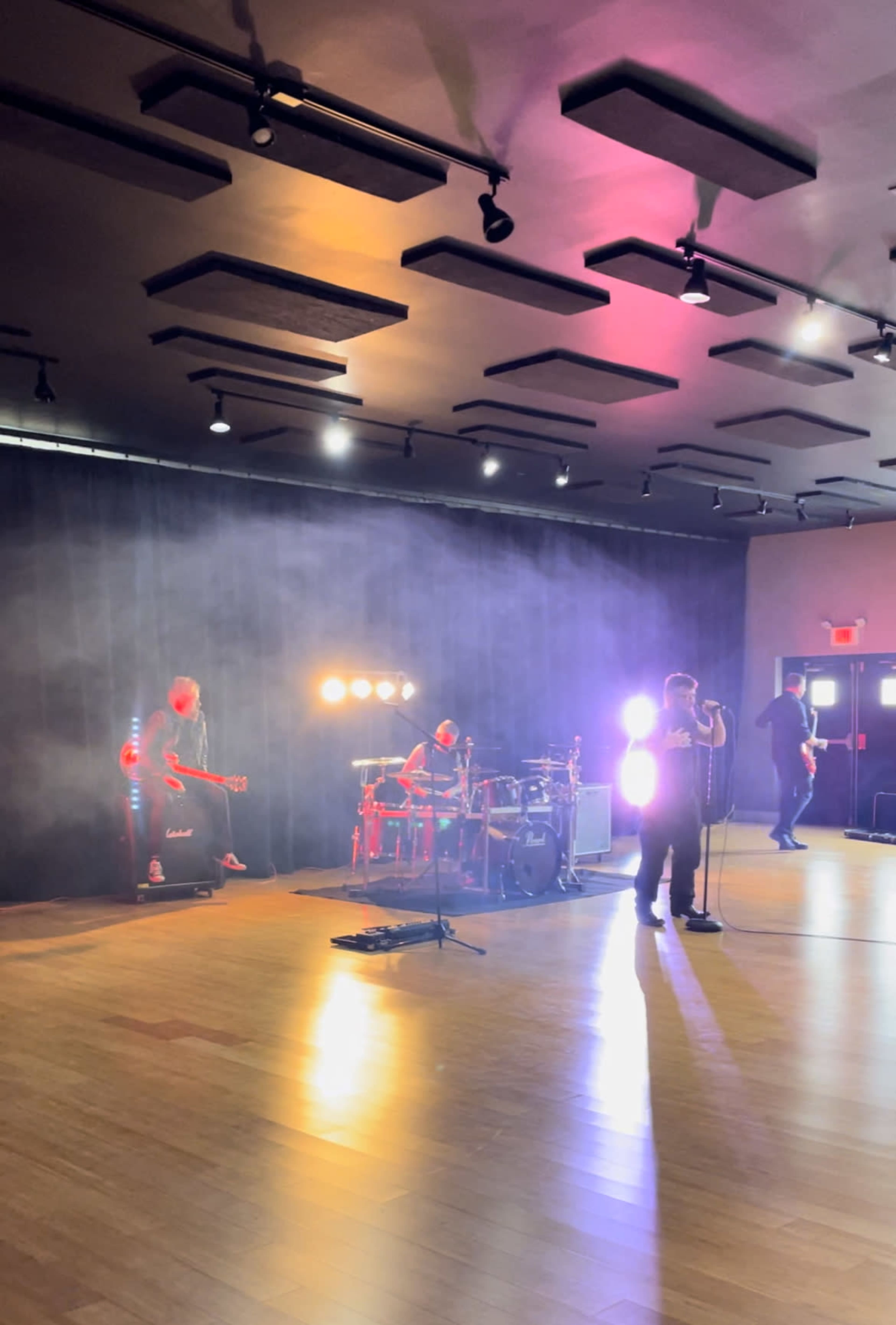 A live band performs on stage with dramatic lighting and a smoke effect in a spacious venue.