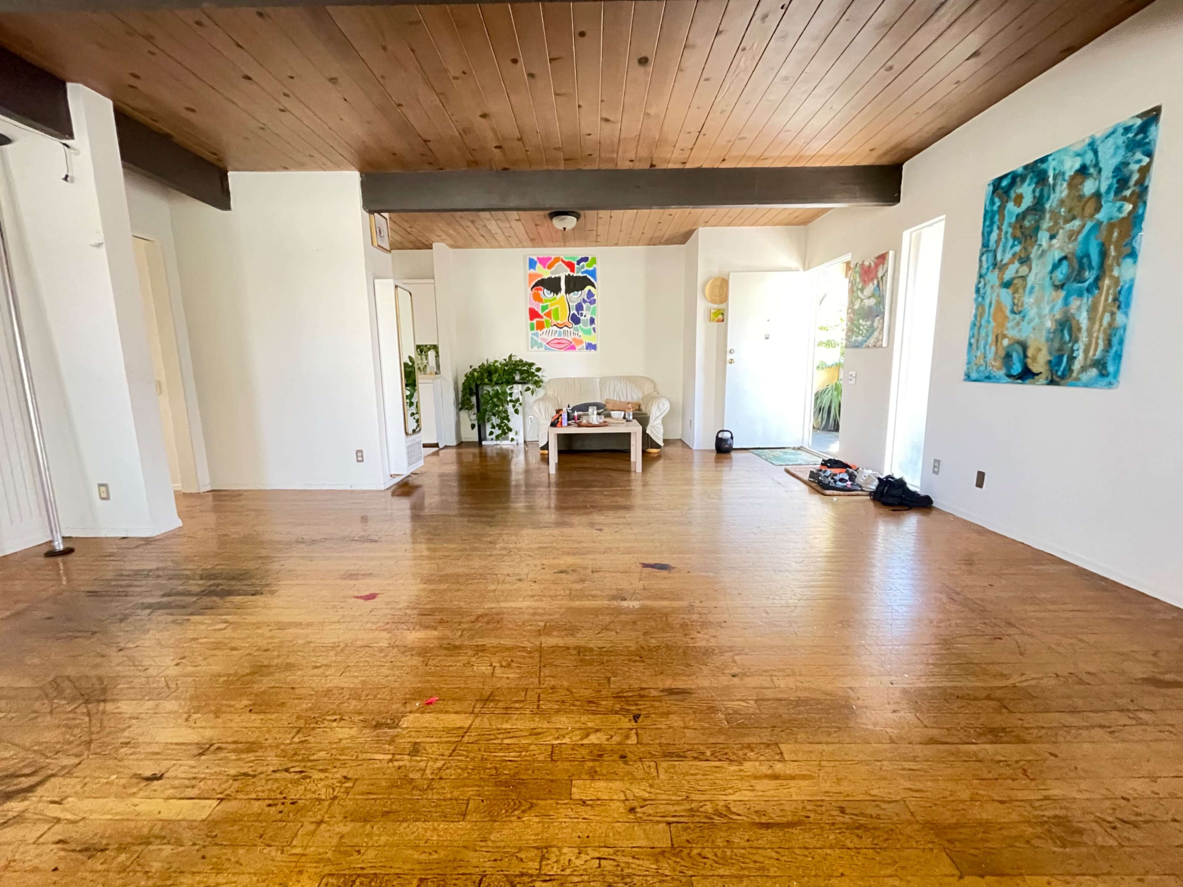 A spacious, empty room with wooden floors, a coffee table in the center, and several pieces of abstract art on the white walls.
