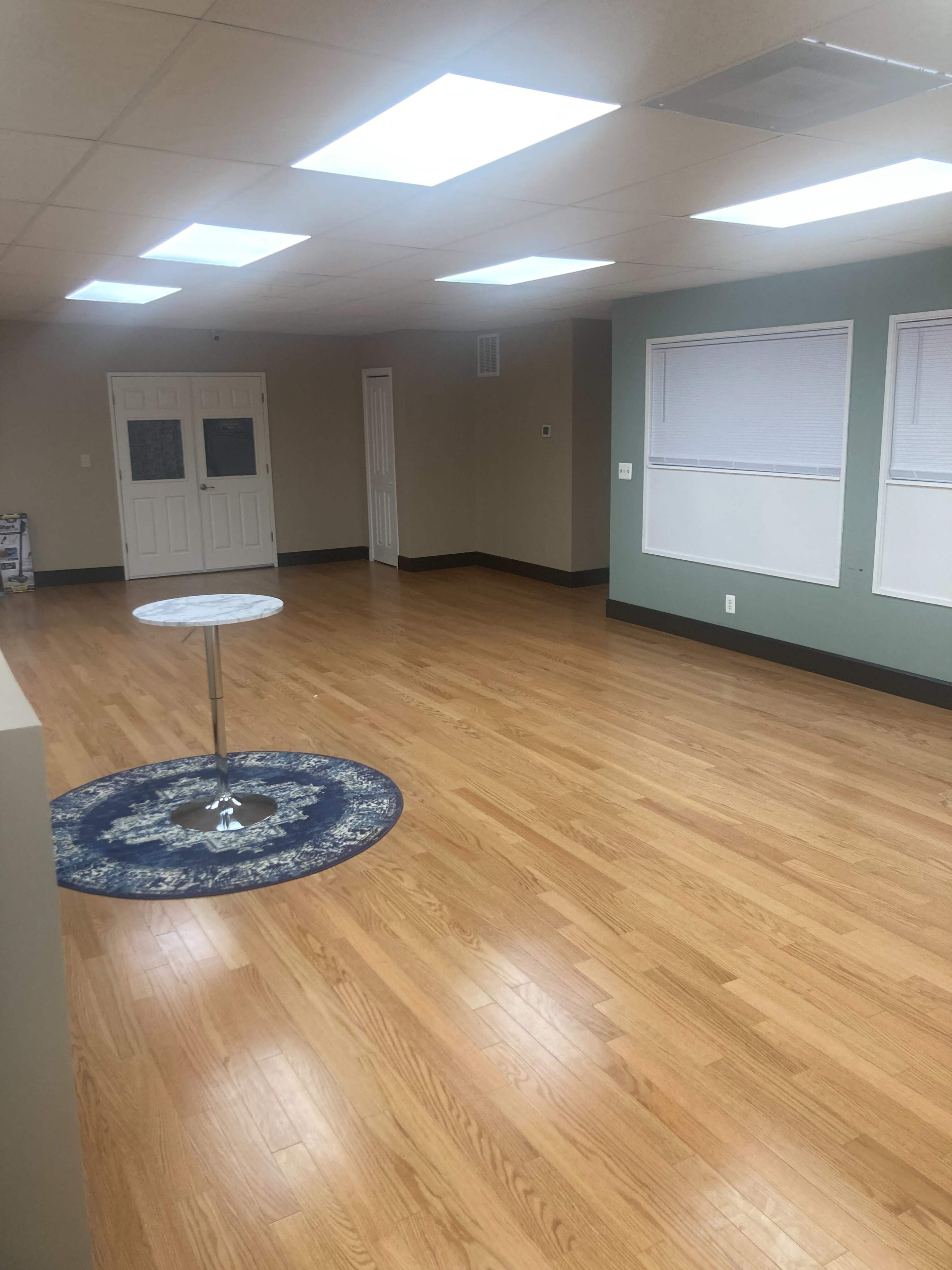 A spacious, empty room with hardwood flooring, a circular rug in the center, and overhead skylights providing natural light.