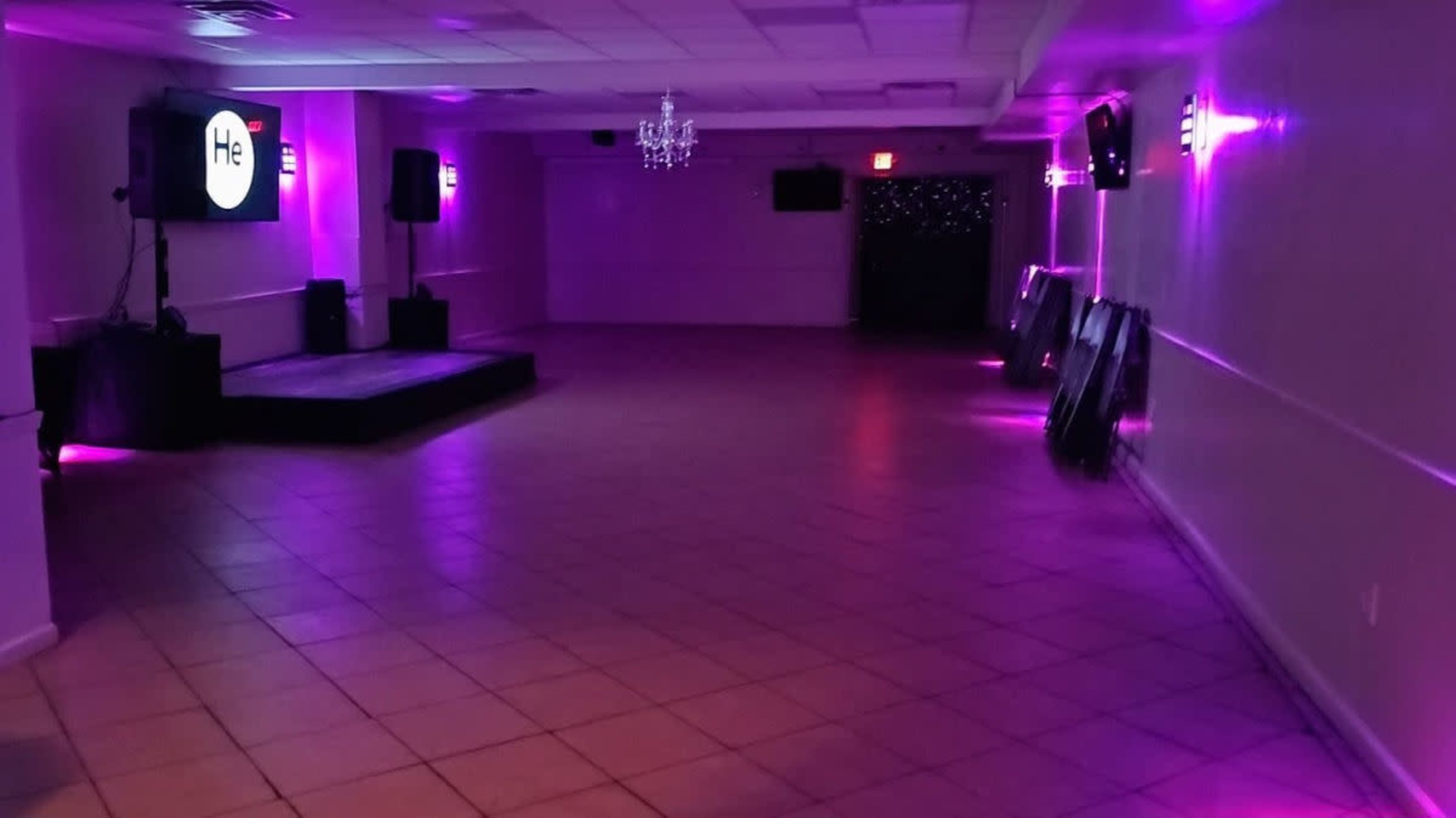 An empty event space with purple lighting, a small stage, and a screen on one wall.