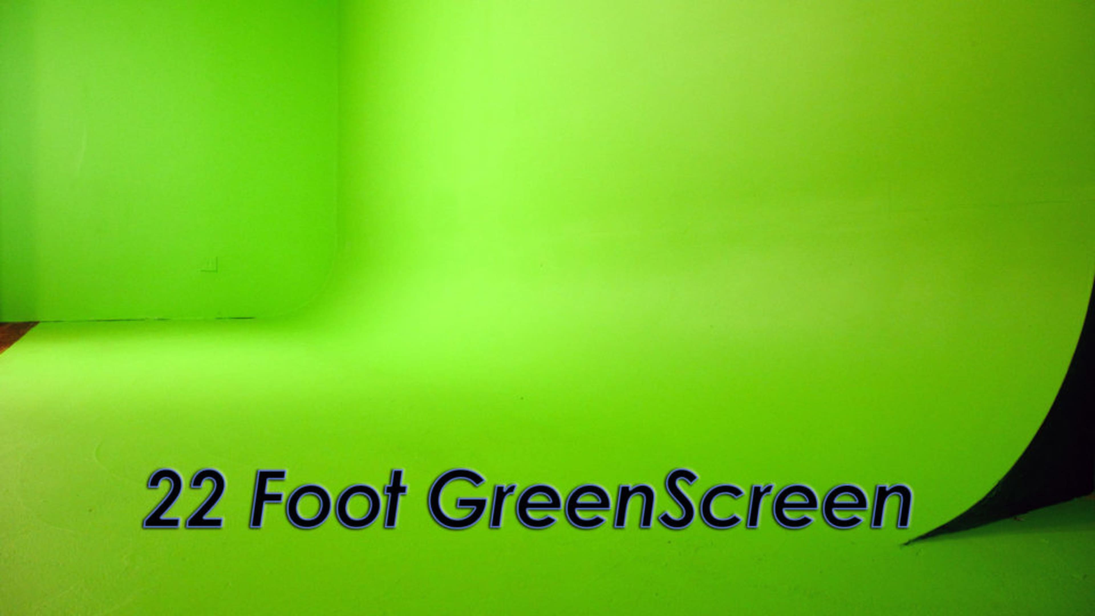 The image shows a bright green studio space featuring a 22-foot green screen seamlessly extending from the floor to the wall.