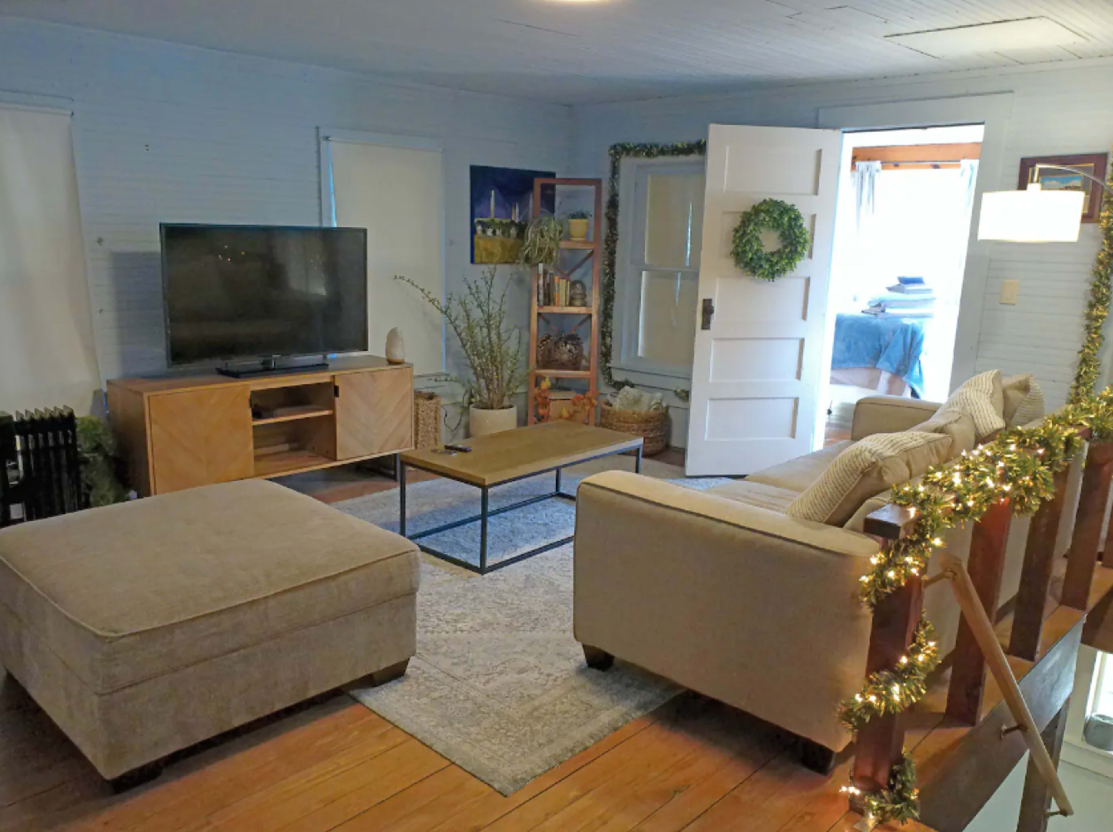 The image shows a living room with a television on one wall, a coffee table in the center, a couch, an ottoman, and a doorway leading to another room.