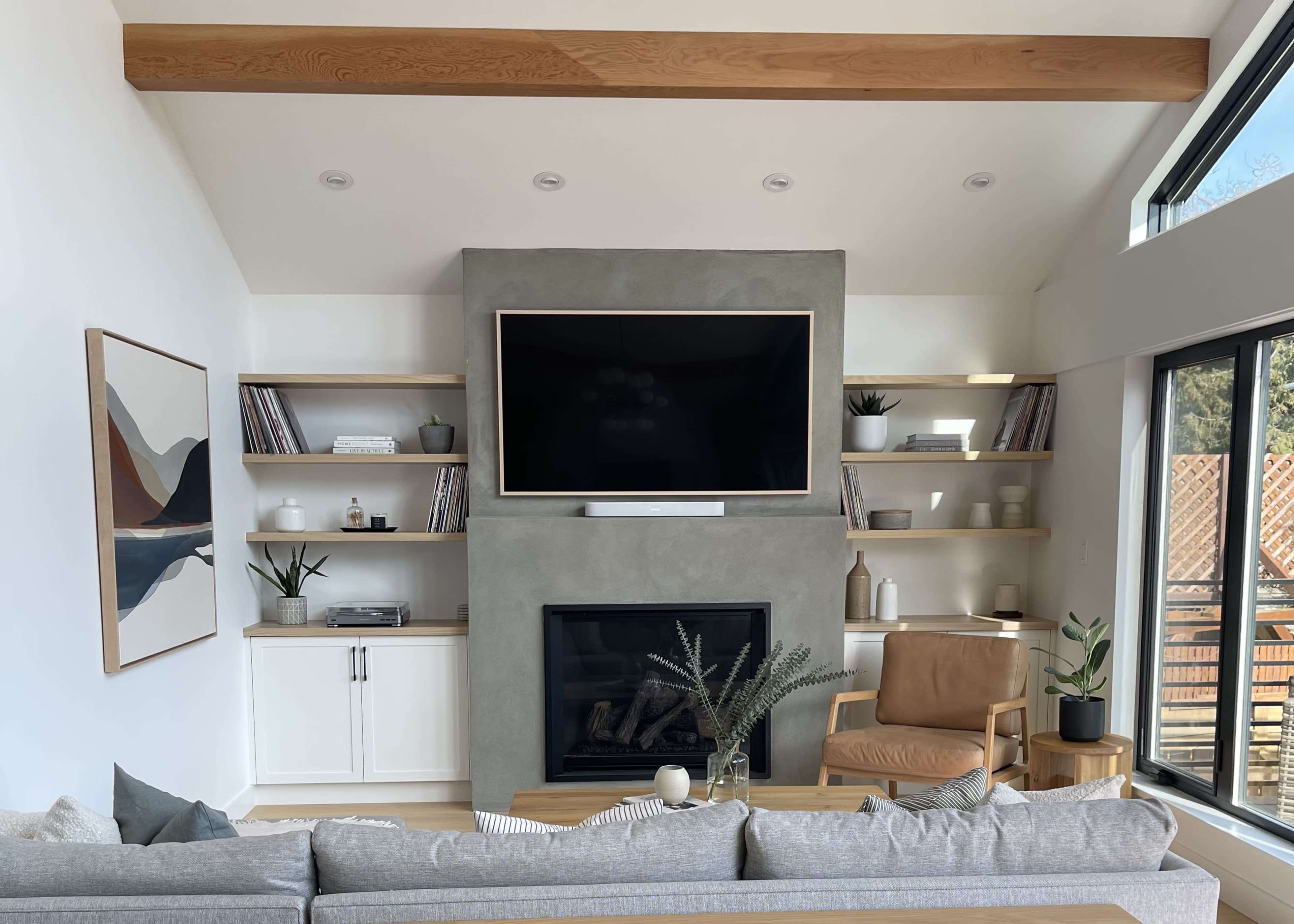 A modern living room featuring a large flat-screen TV mounted above a minimalist fireplace, flanked by wooden shelves filled with decorative items and books.