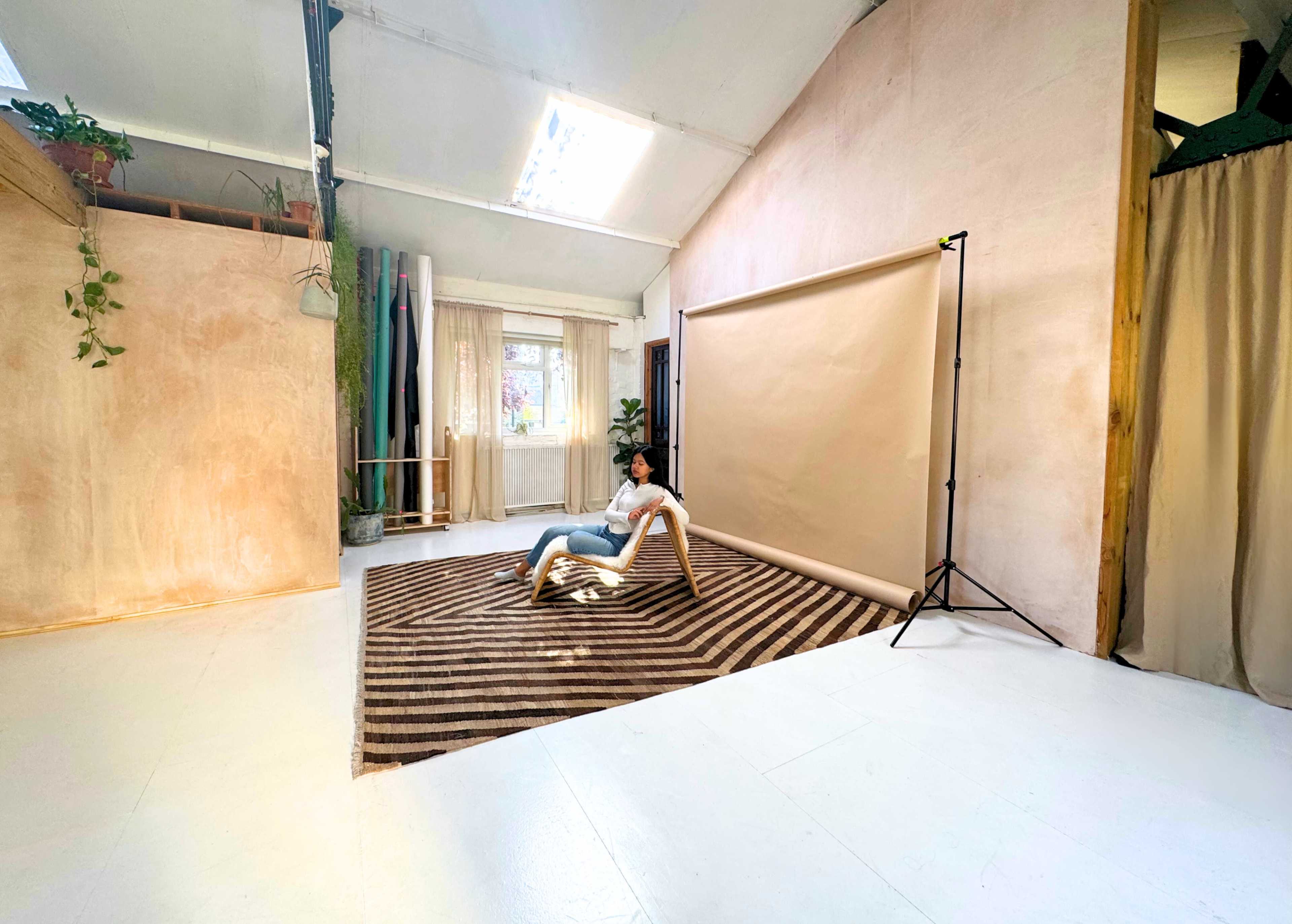 A person is sitting on a chair in a spacious studio with a striped rug, soft lighting, and neutral-colored walls.