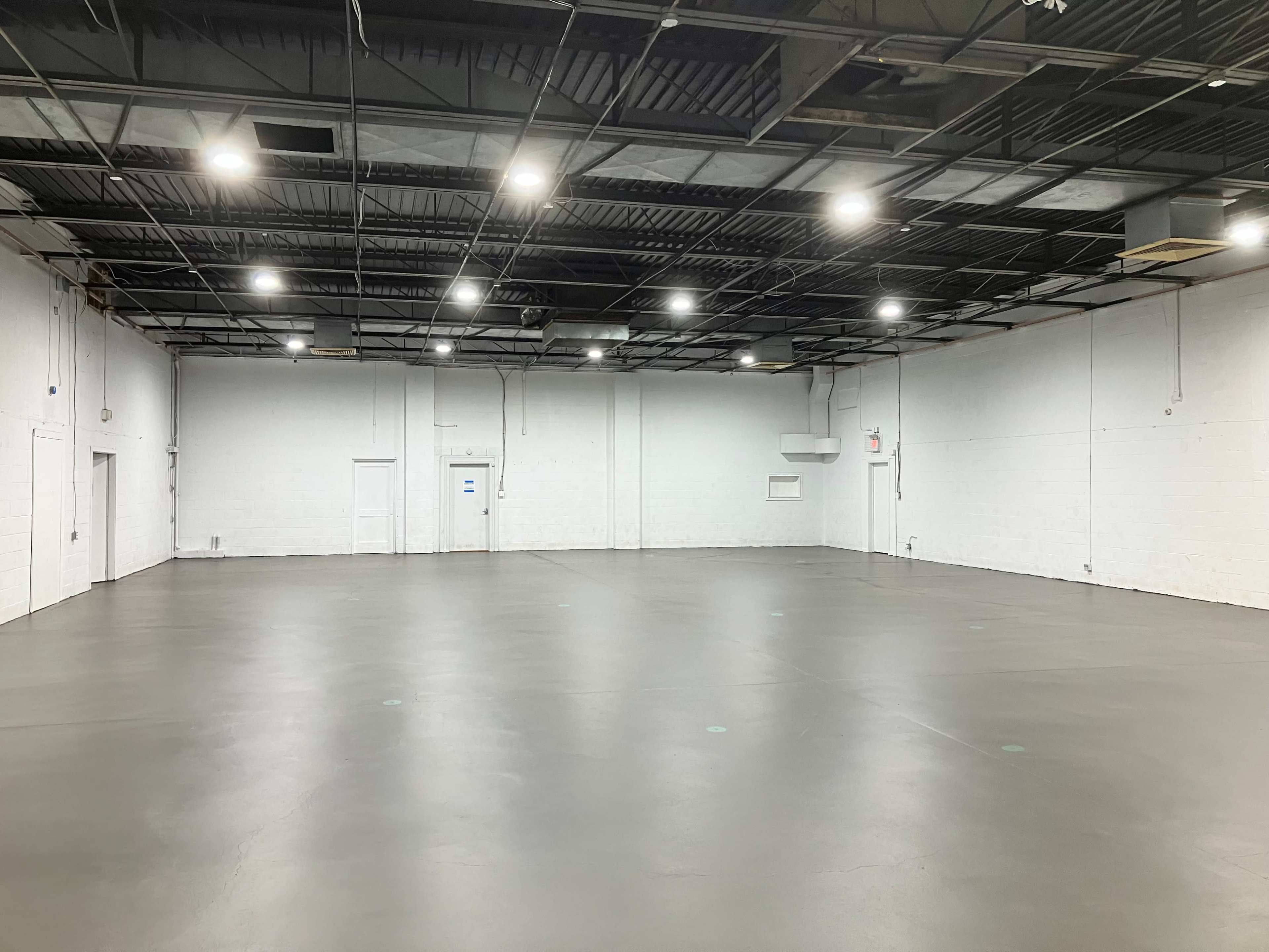 The image shows a spacious, empty warehouse with concrete flooring and exposed ceiling beams.
