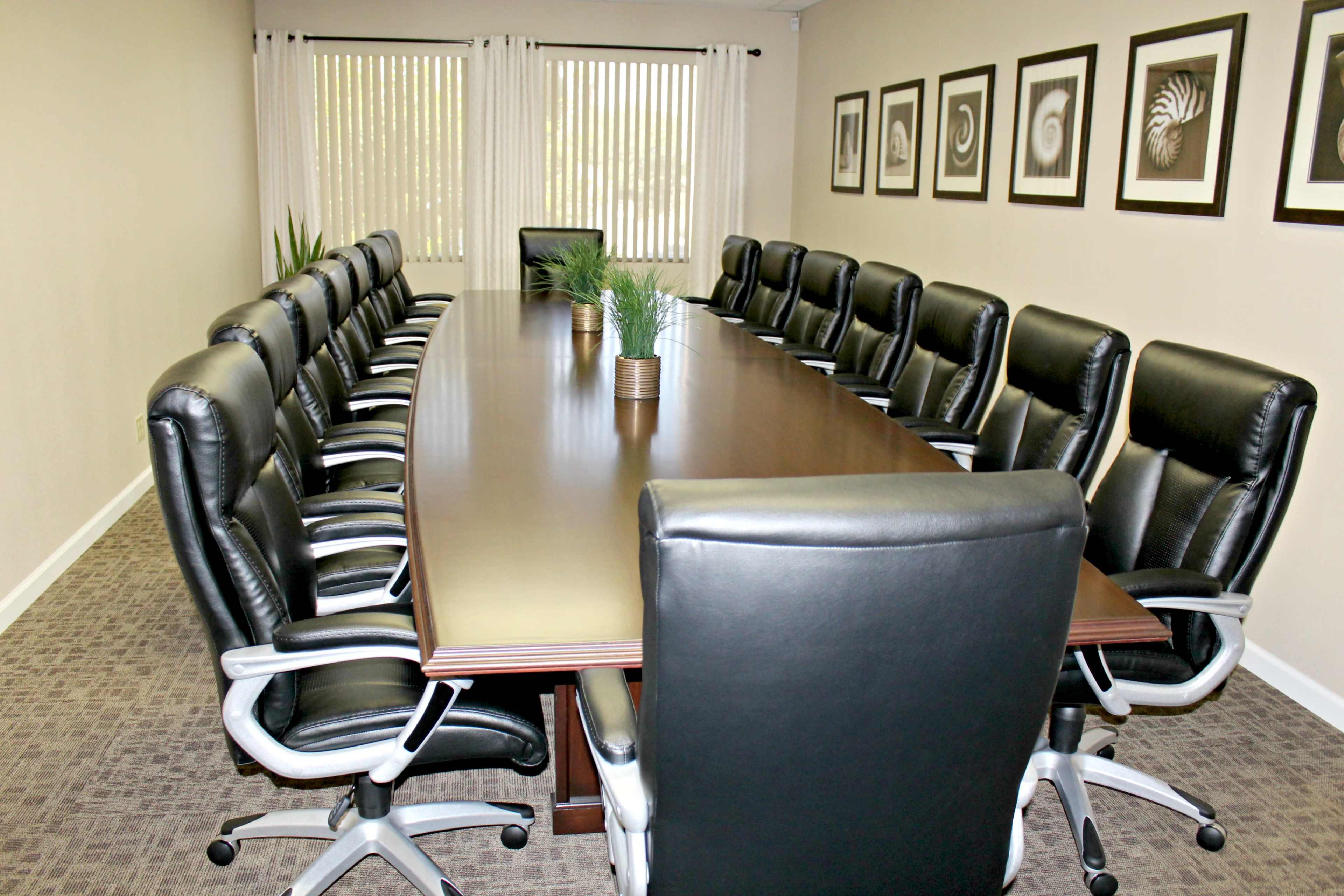 A large conference room features a long wooden table surrounded by black leather chairs and decorated with framed artworks on the walls.