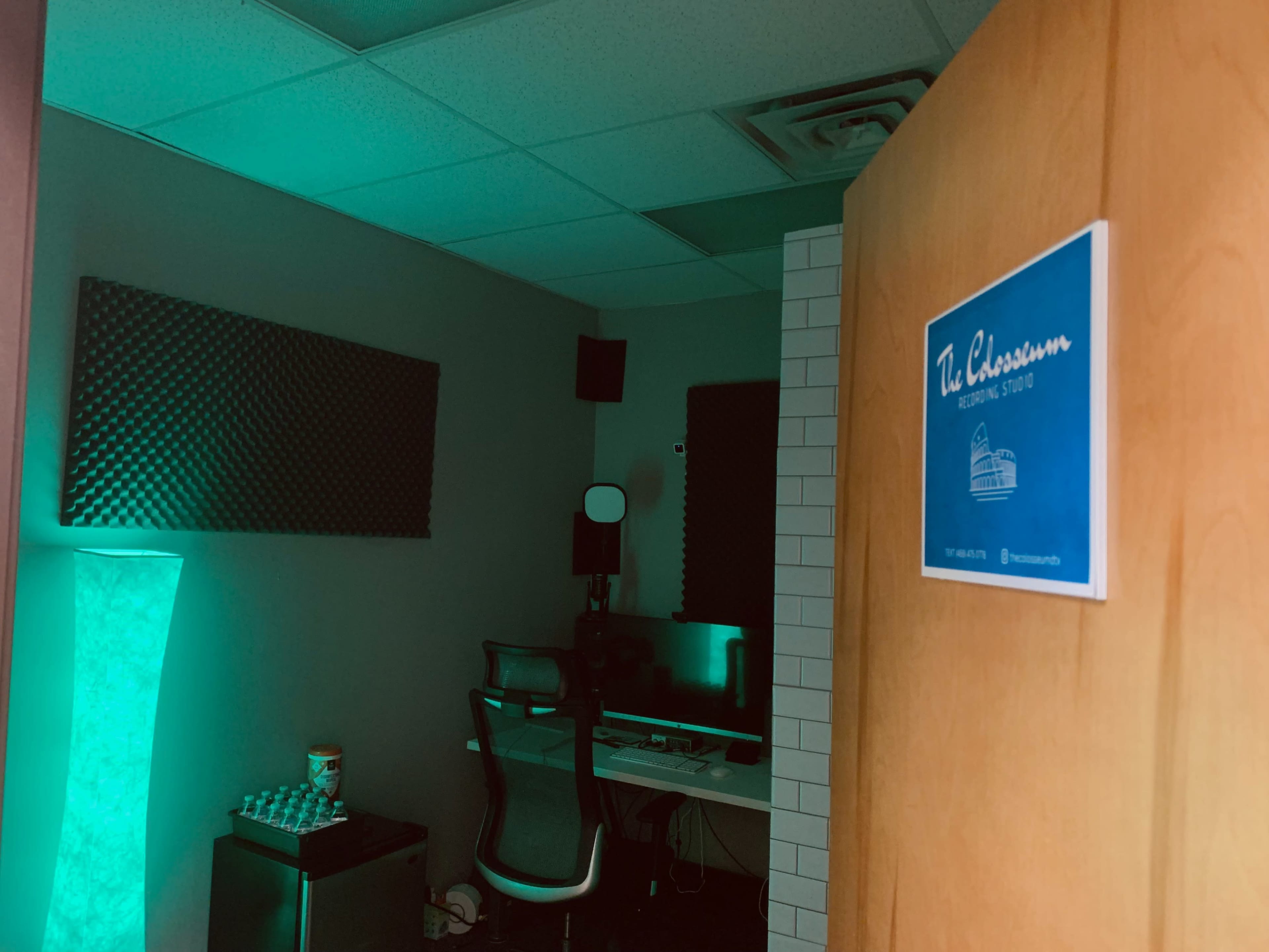 A classroom with a computer workstation is seen through a partially open door, illuminated by green lighting.