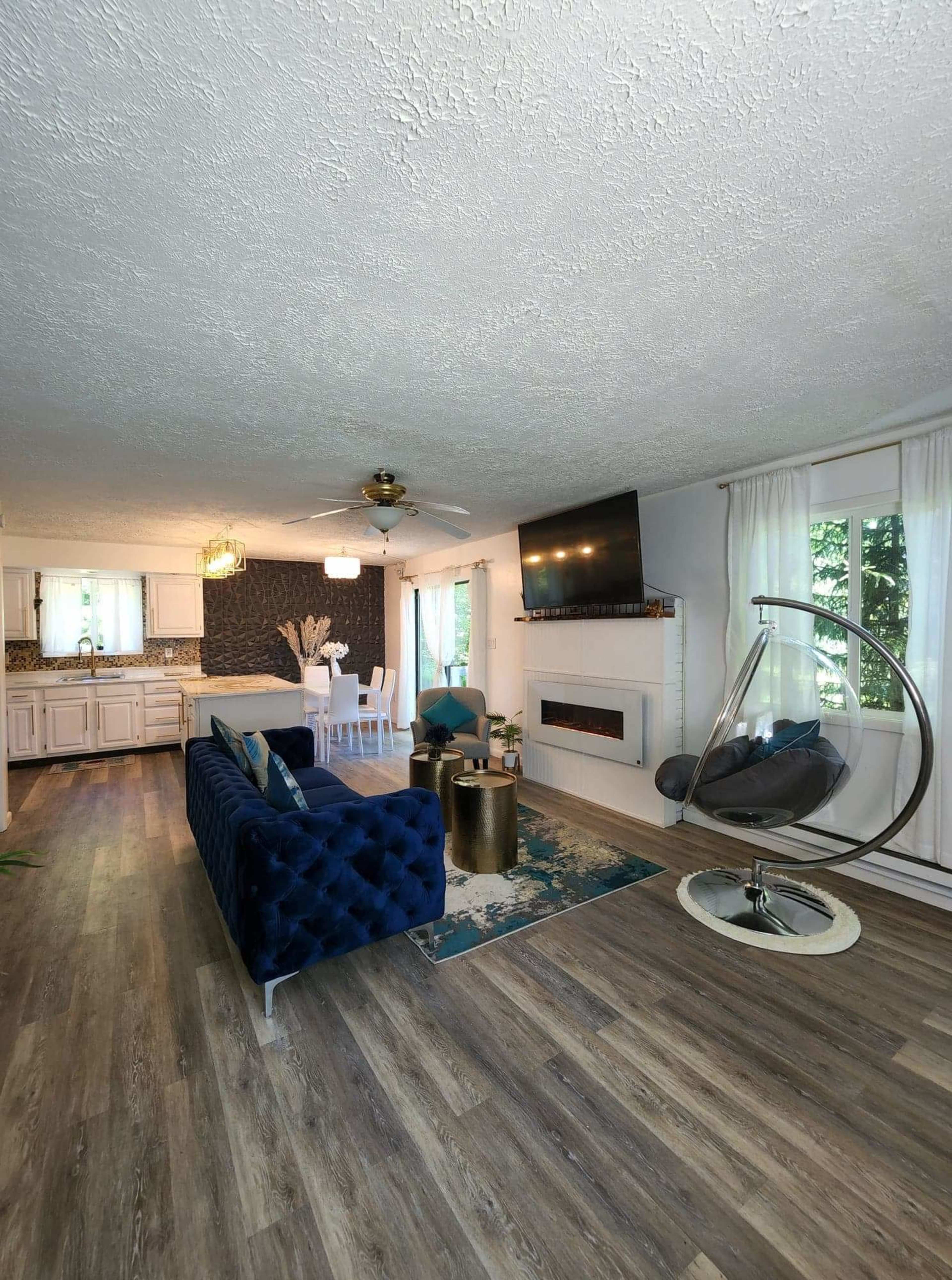 A modern living room featuring a blue velvet sofa, a hanging chair, and a flat-screen TV mounted above an electric fireplace.