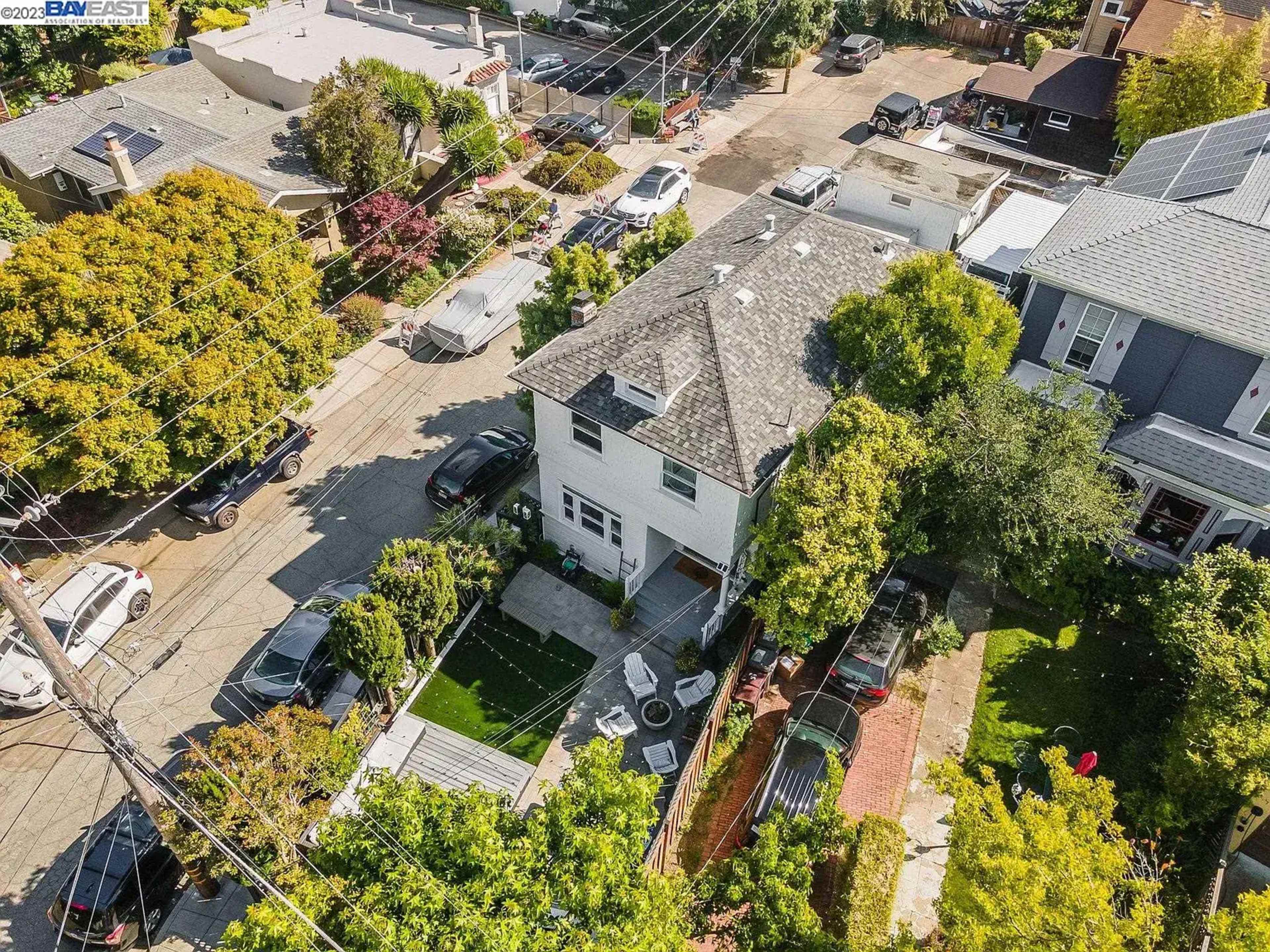 An aerial view of a residential neighborhood featuring multiple houses, parked cars, and green trees.