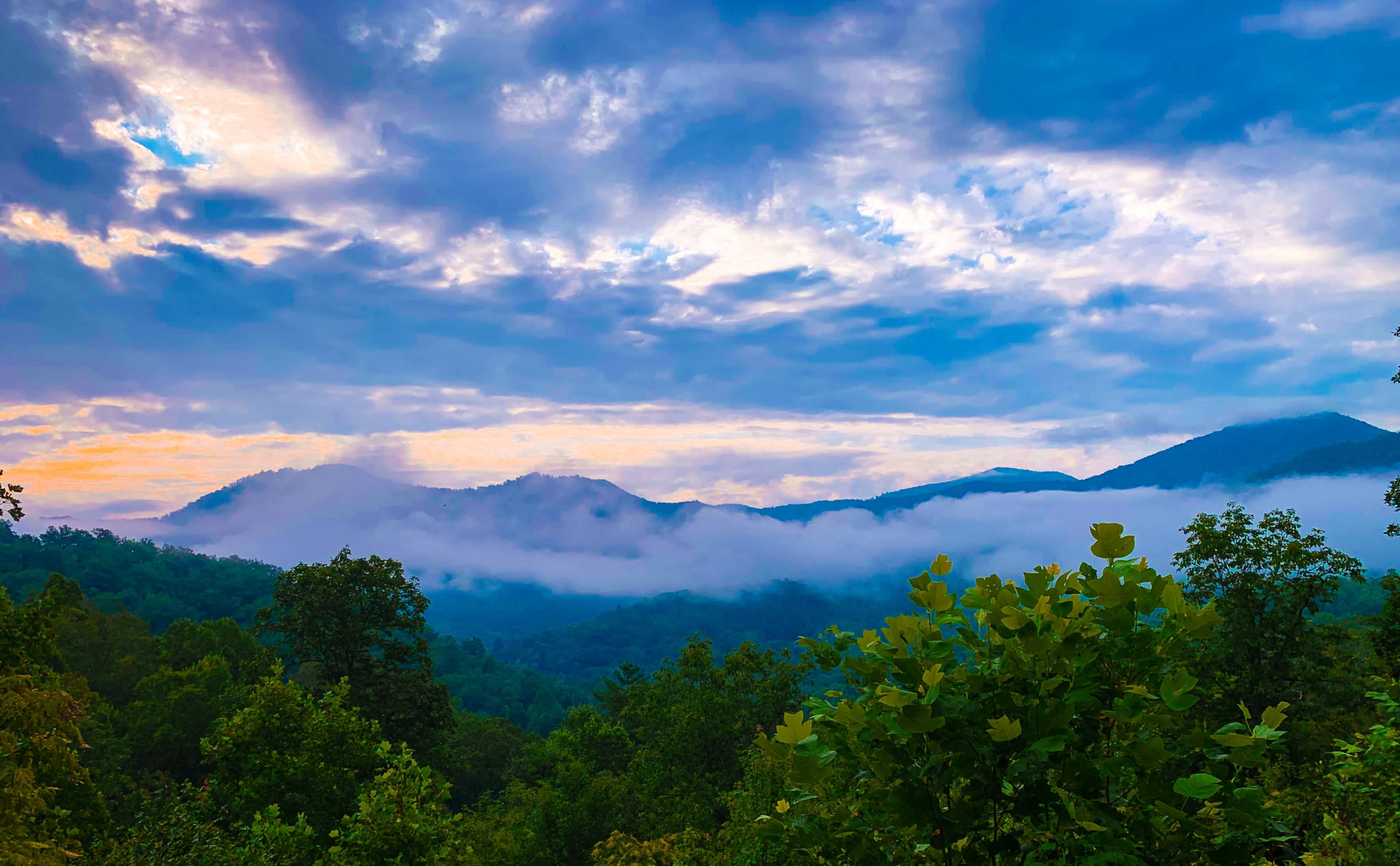 A panoramic view of mountains shrouded in fog under a cloudy sky at dawn.