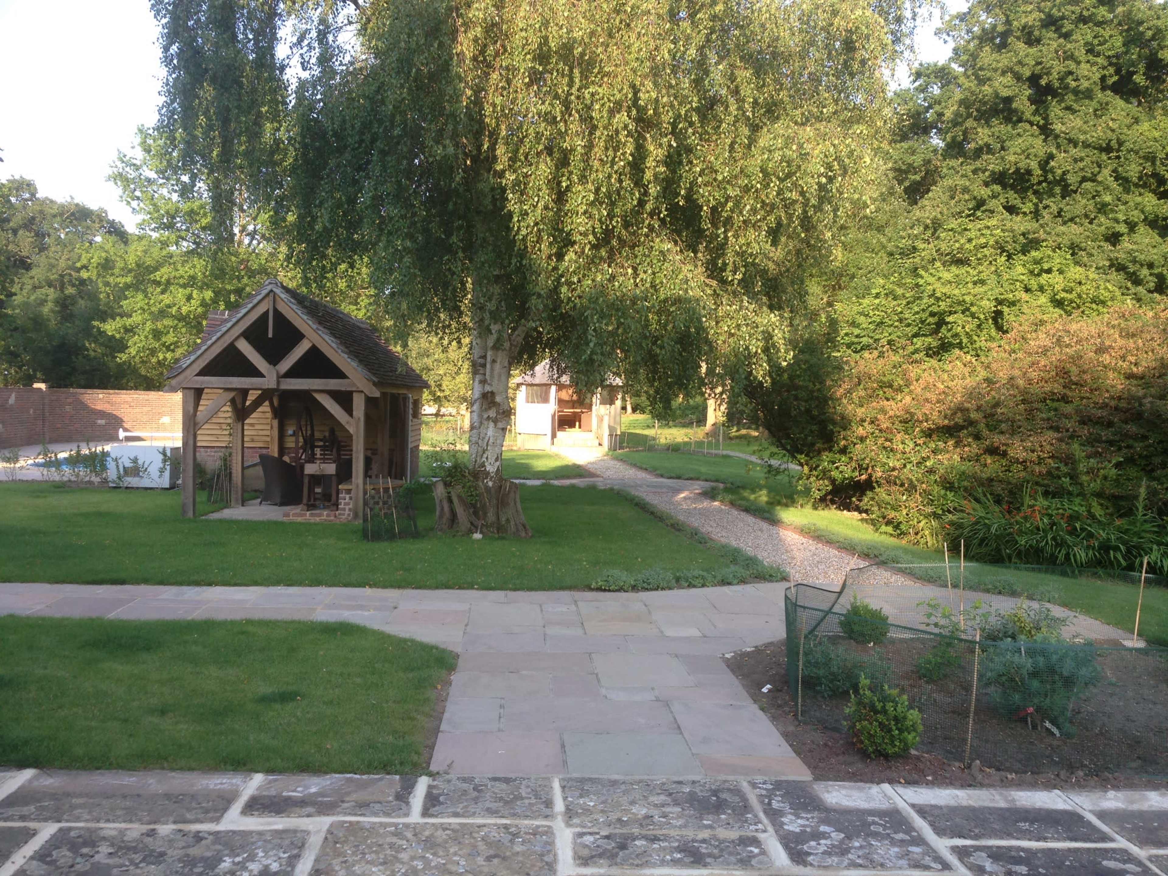 A garden with a wooden gazebo, a pathway, and lush greenery surrounding the area.