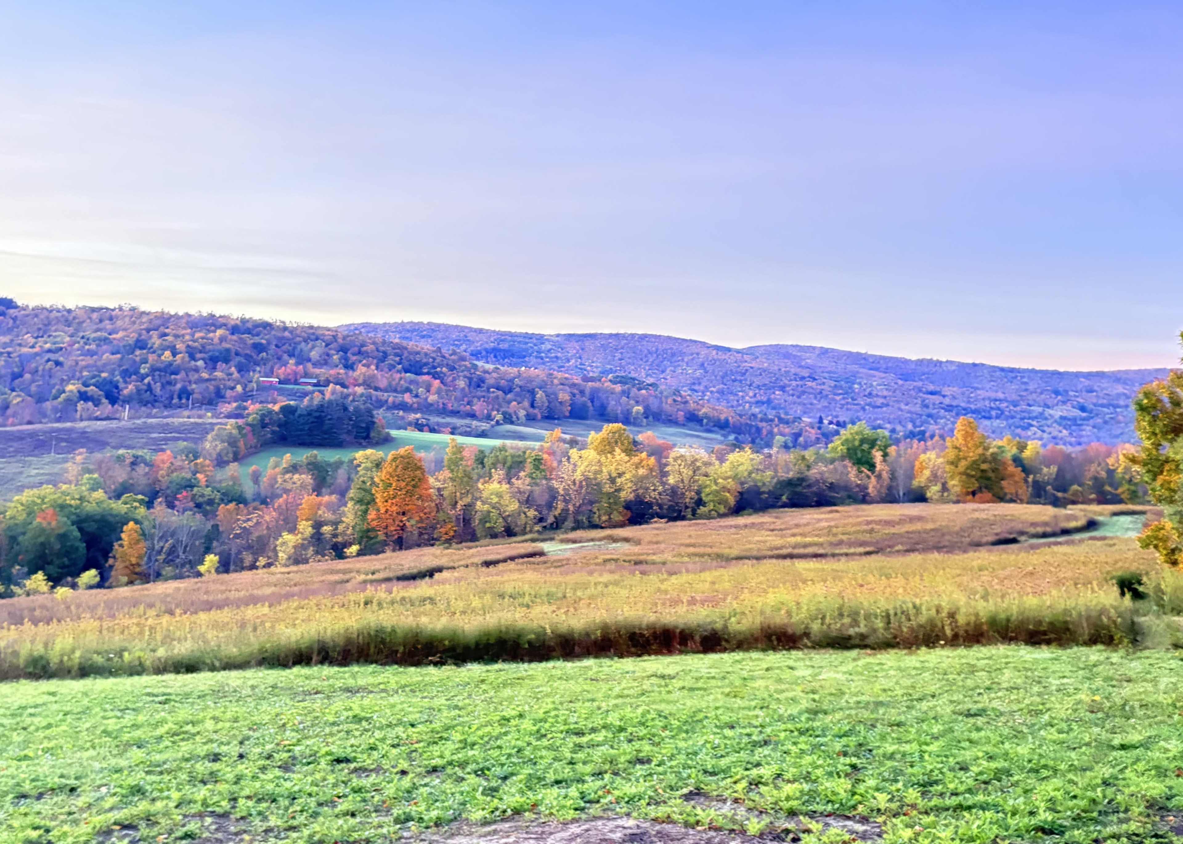 The image shows a scenic landscape with rolling hills covered in autumn foliage and a clear sky above.