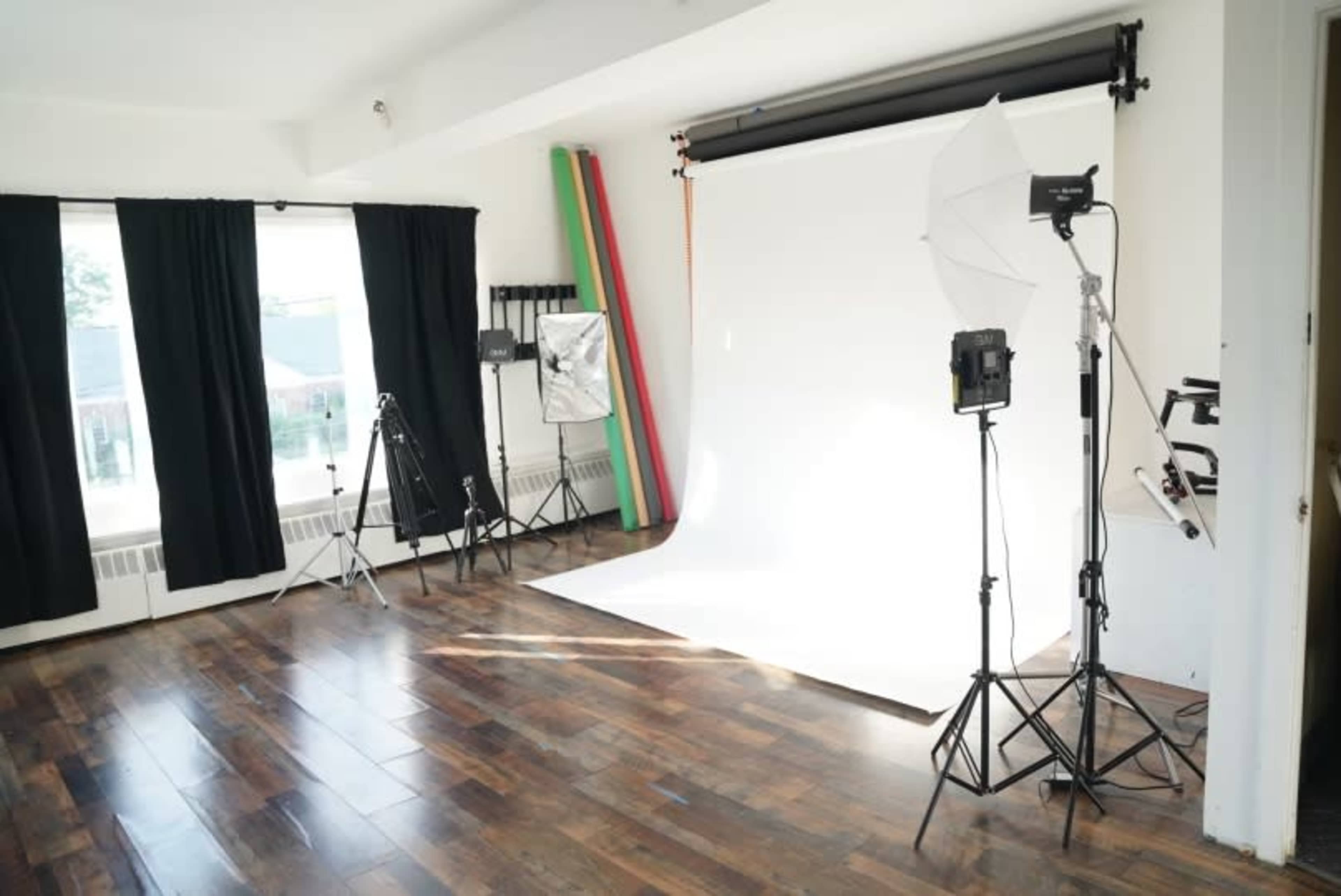 A photography studio with various equipment, including lights, backdrops, and tripods, set up on a hardwood floor.