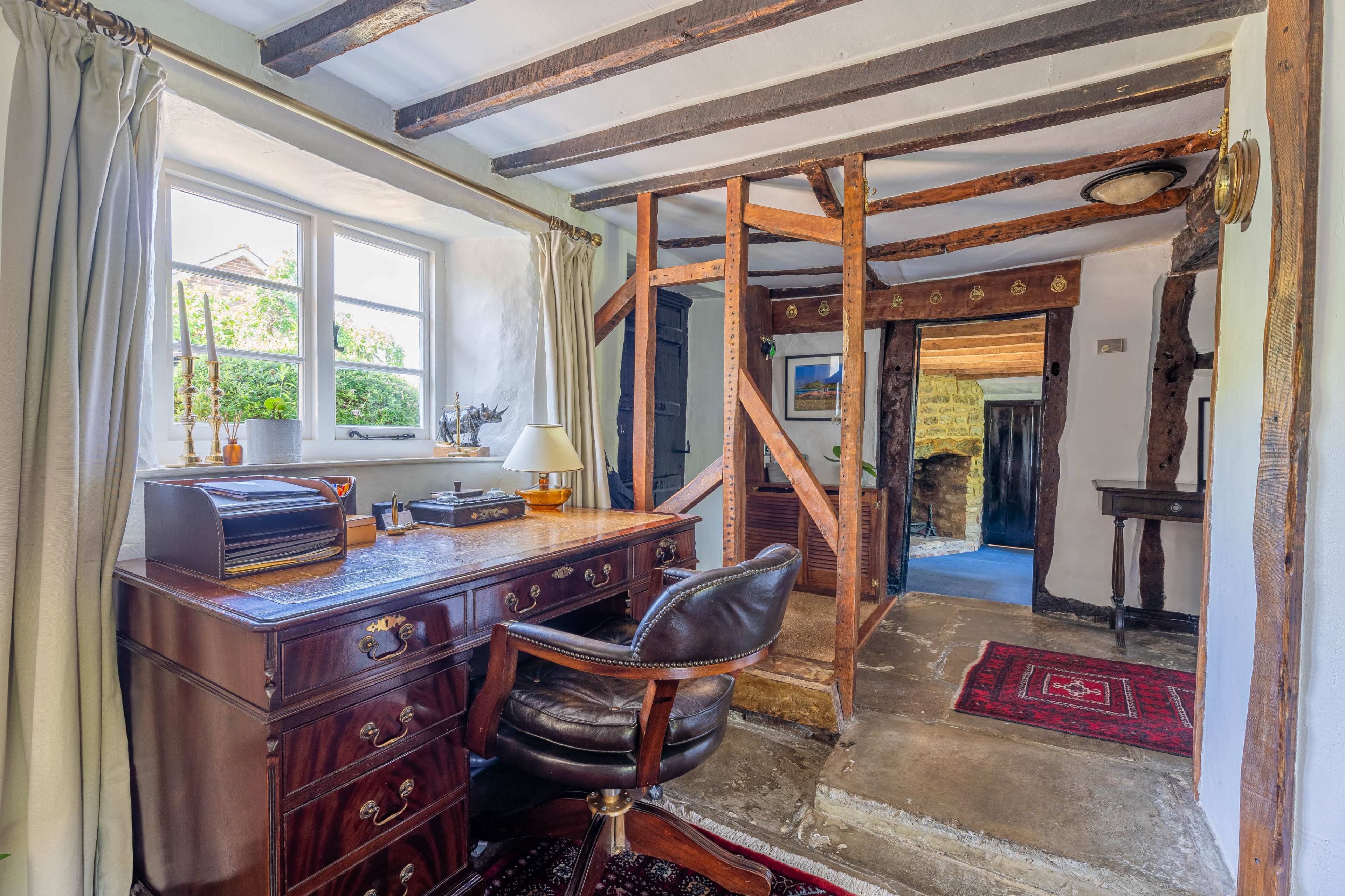 A rustic interior with a wooden desk and chair, a window letting in natural light, and exposed wooden beams in the ceiling.