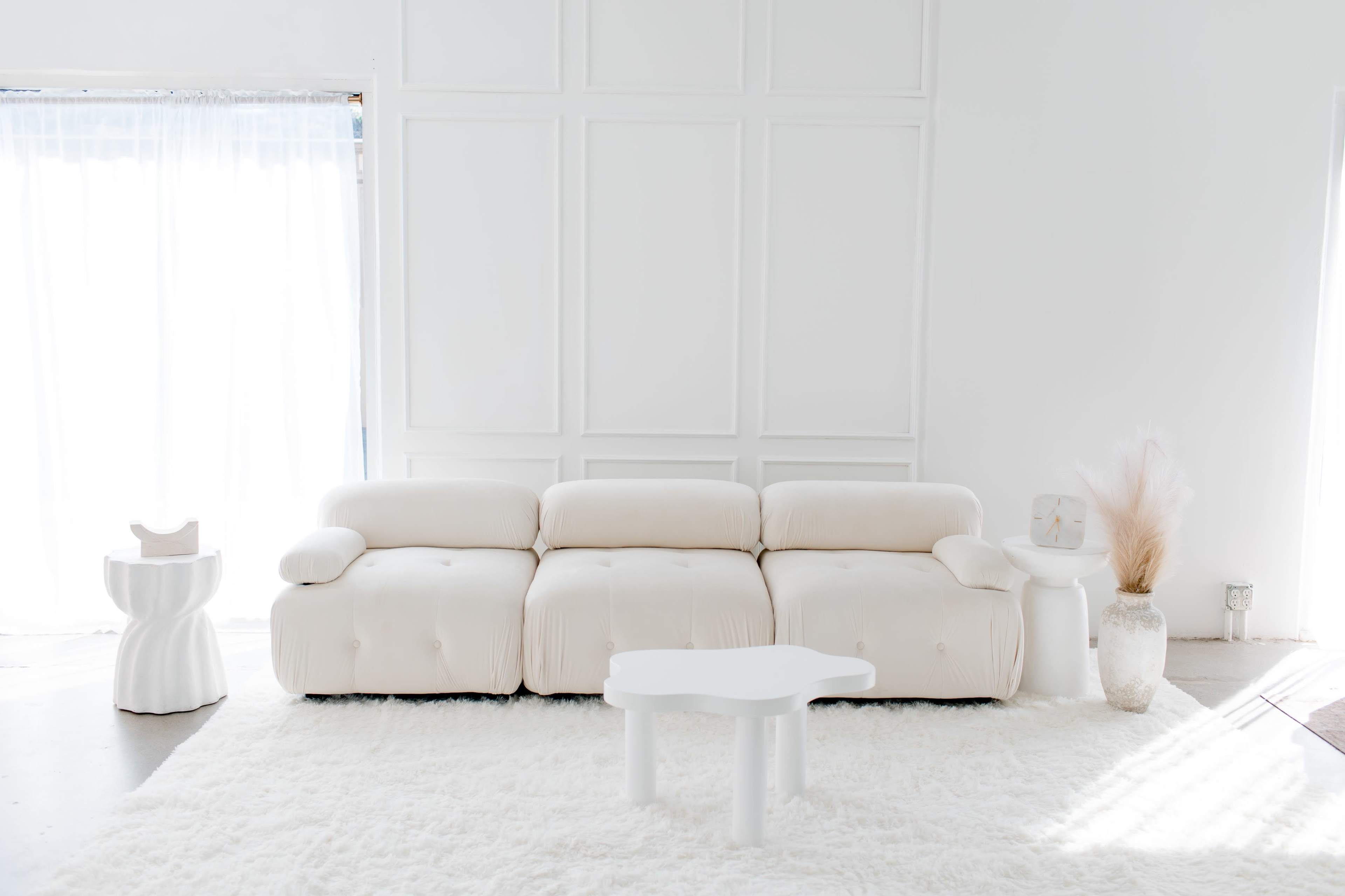 A light-colored, contemporary sofa set in a bright room with a white rug, a small side table, and minimalist decor elements.