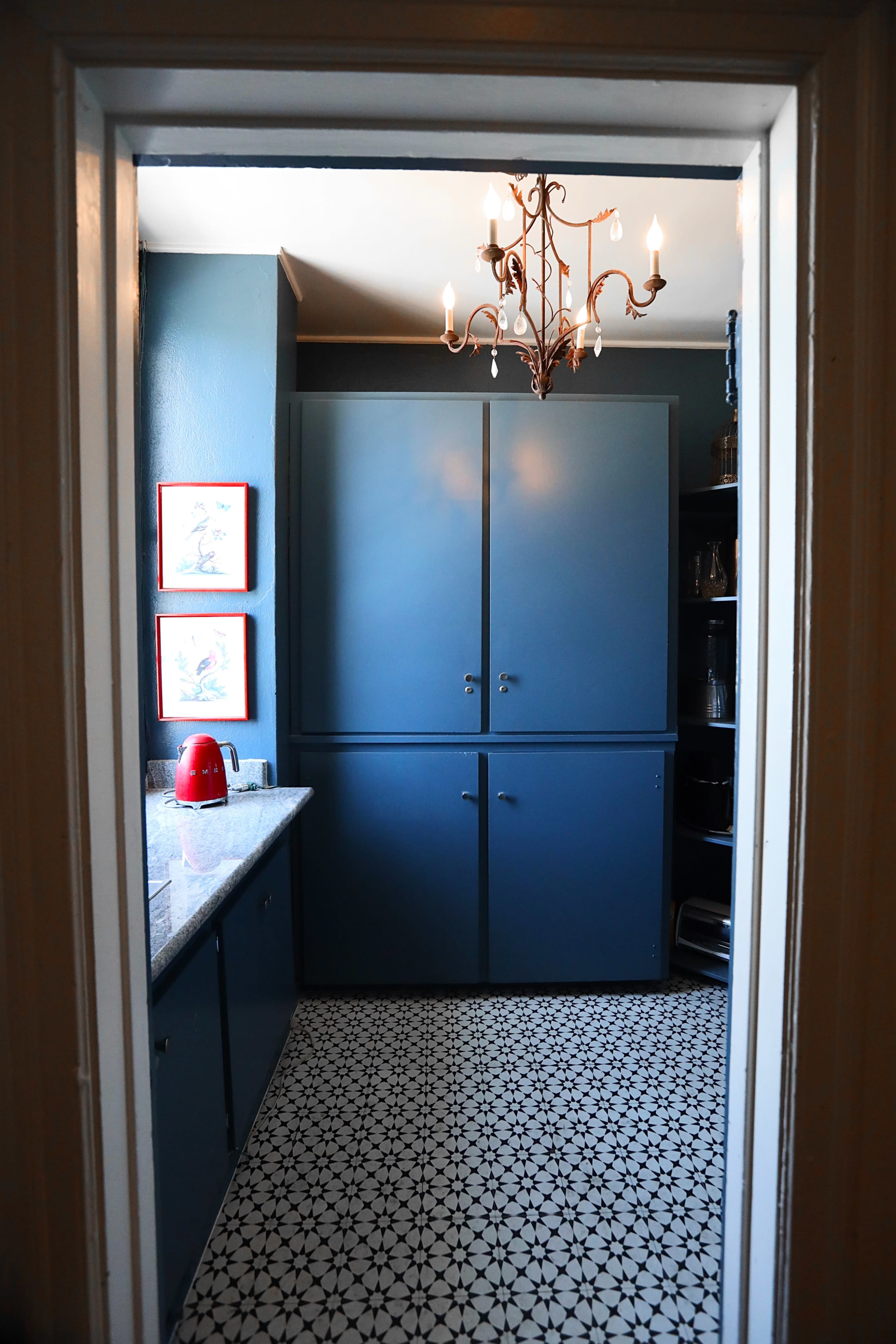 A small kitchen features blue cabinets, a granite countertop, and black-and-white patterned tile flooring.