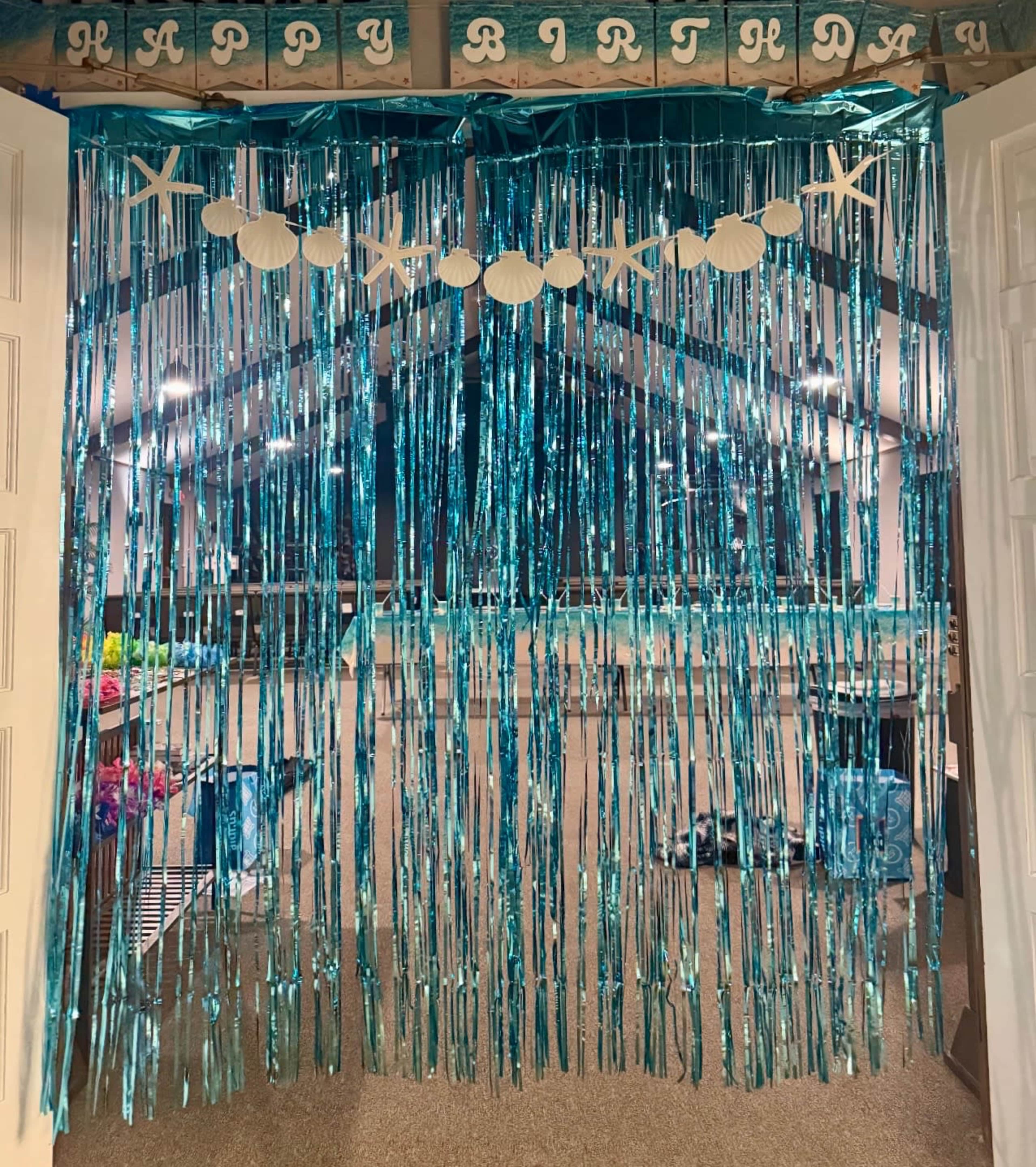 A shimmering blue backdrop with hanging strands and circular cutouts is set up as a birthday decoration at an entrance.