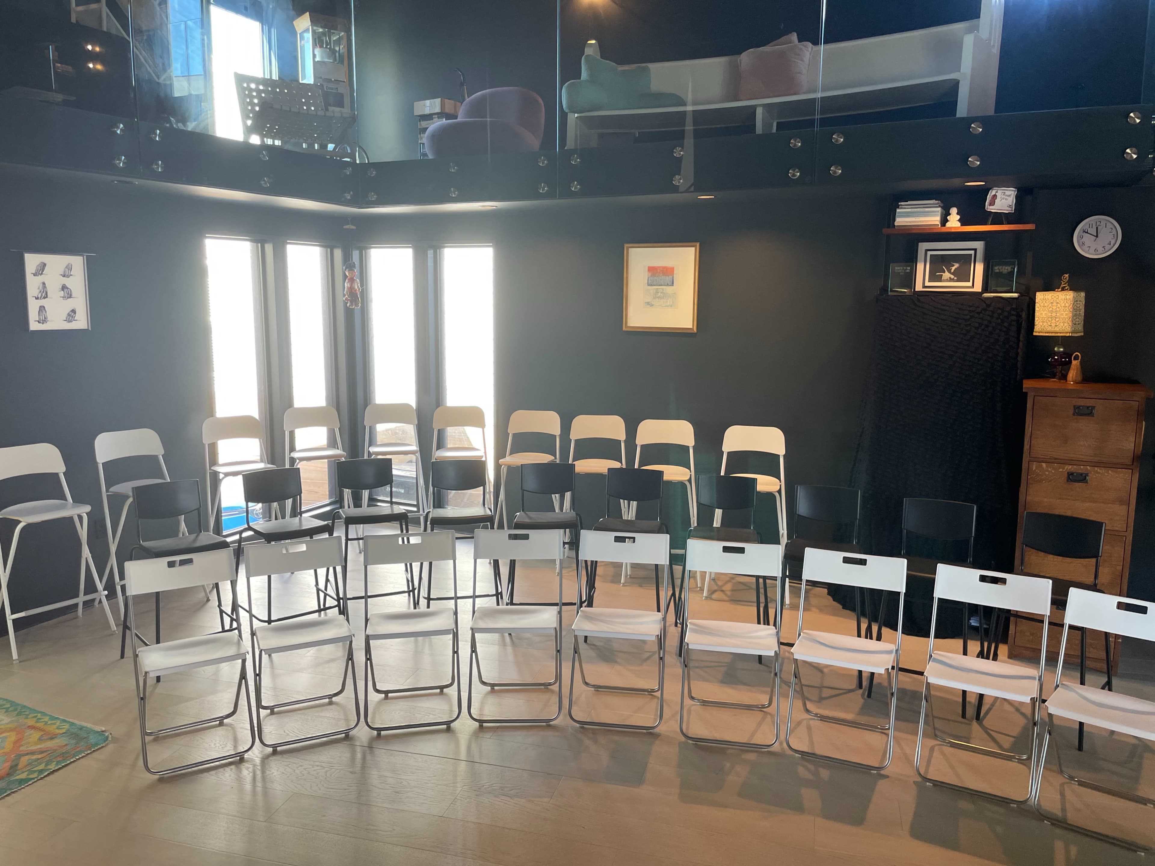 A room arranged with two sets of folding chairs in rows, facing a wall with windows and a decorative piece.