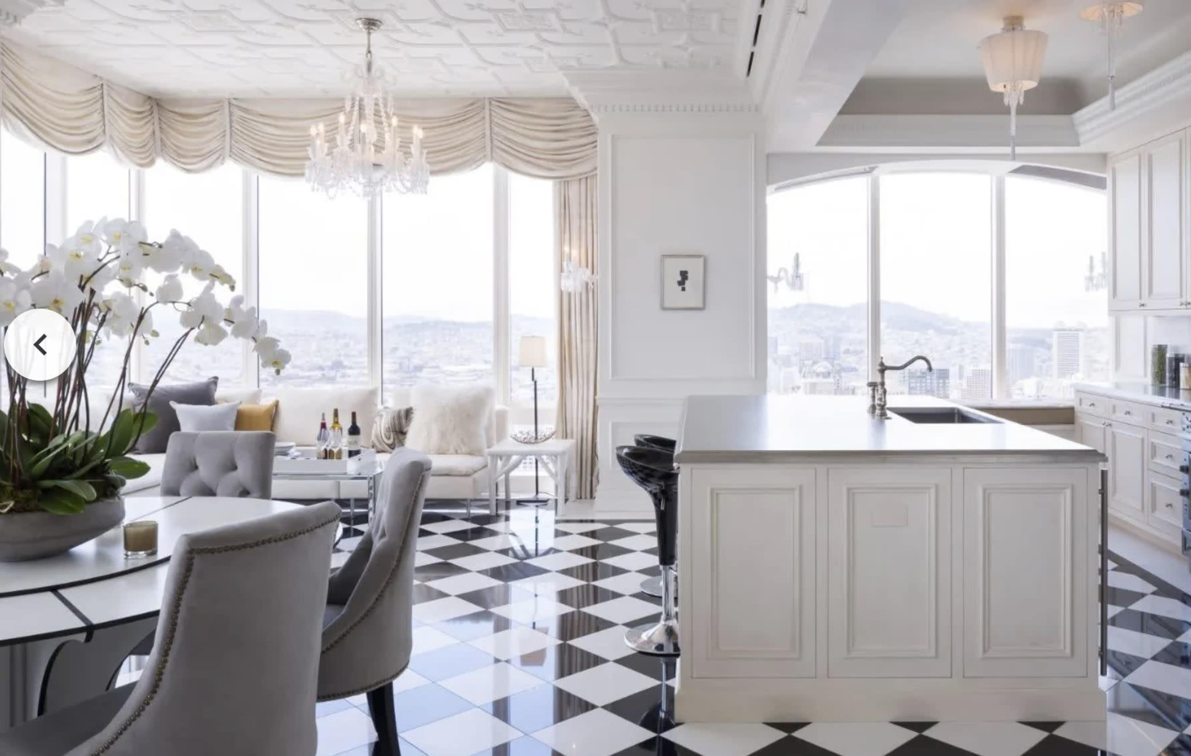 A modern kitchen and dining area with large windows offering a city view, featuring a black-and-white checkered floor and elegant furnishings.