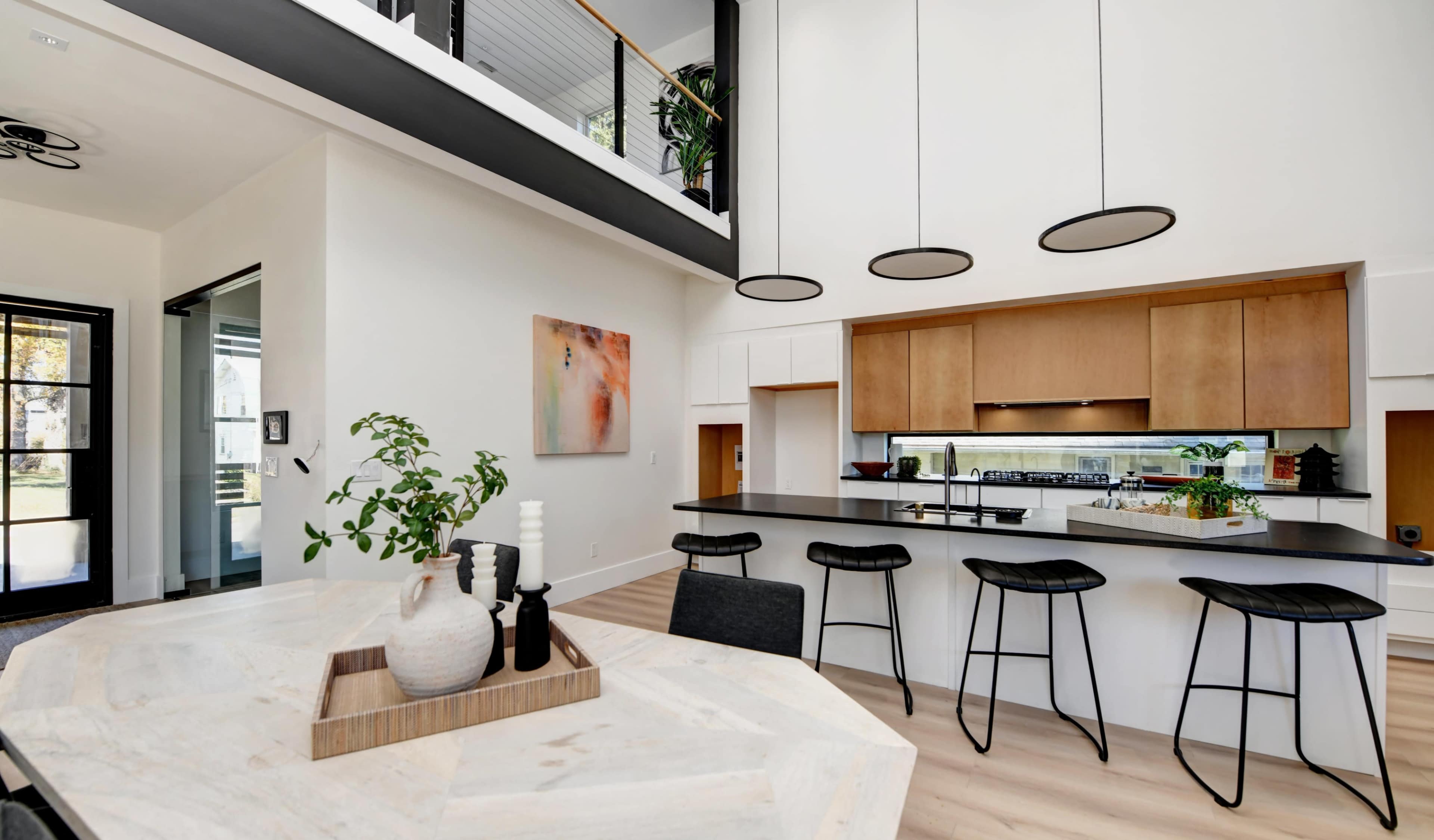 A modern kitchen features a sleek island with bar stools, surrounded by light-colored wood cabinetry and large windows.