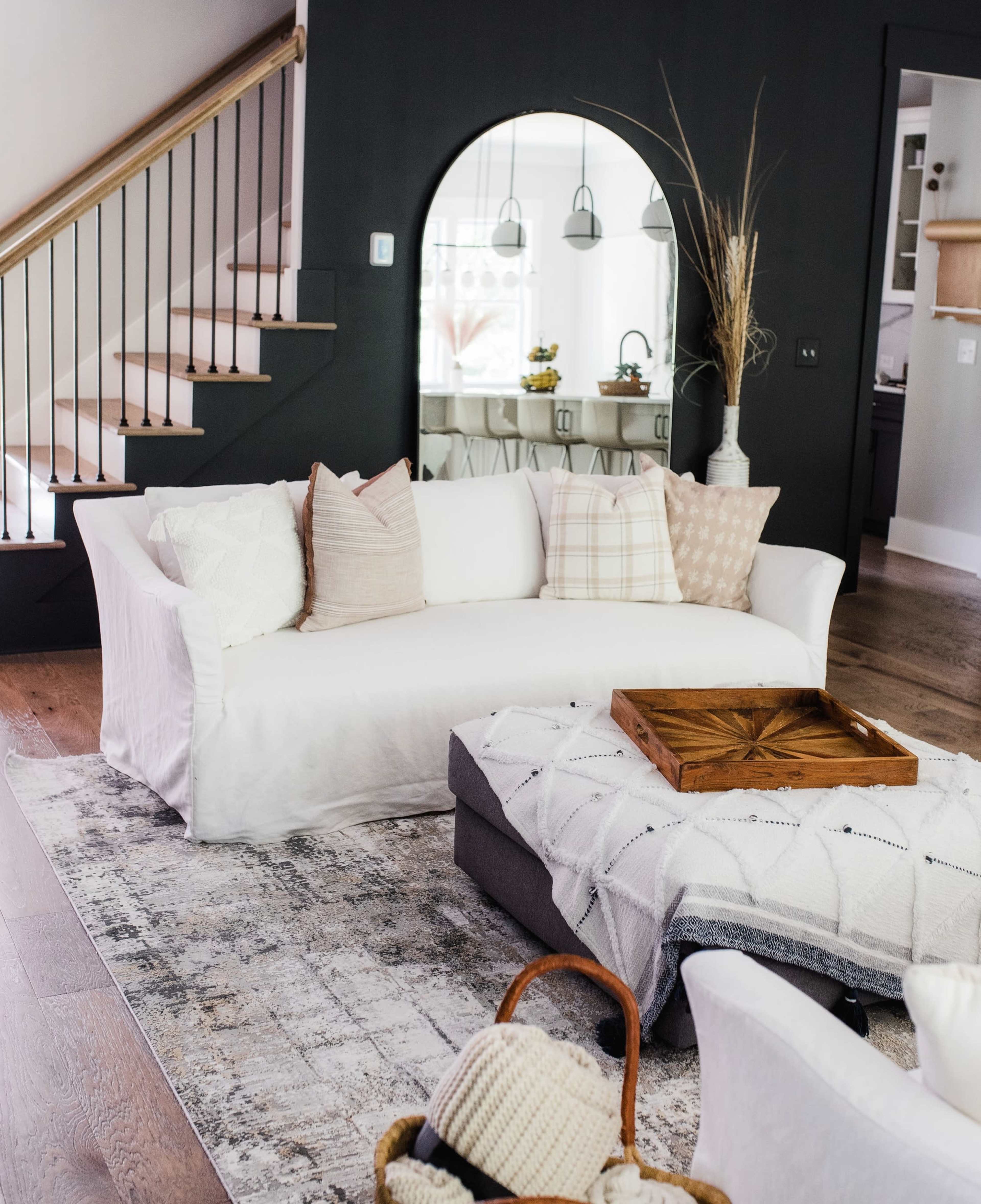 A modern living room featuring a white sofa with decorative pillows, a wooden coffee table, and a patterned area rug under a staircase.