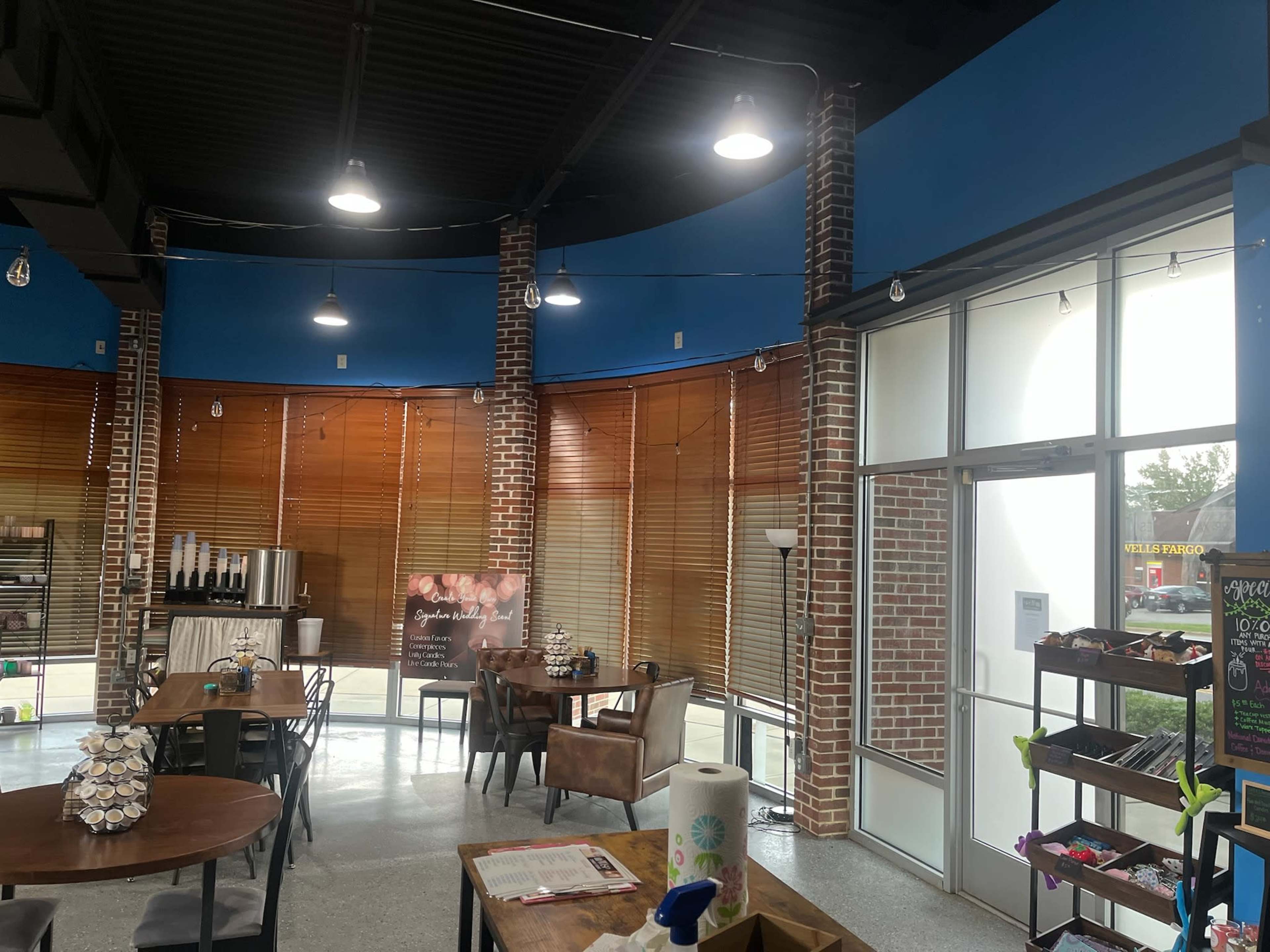 The image shows a modern café interior with brick walls, blue accents, wooden blinds, and several tables and chairs arranged in a well-lit space.