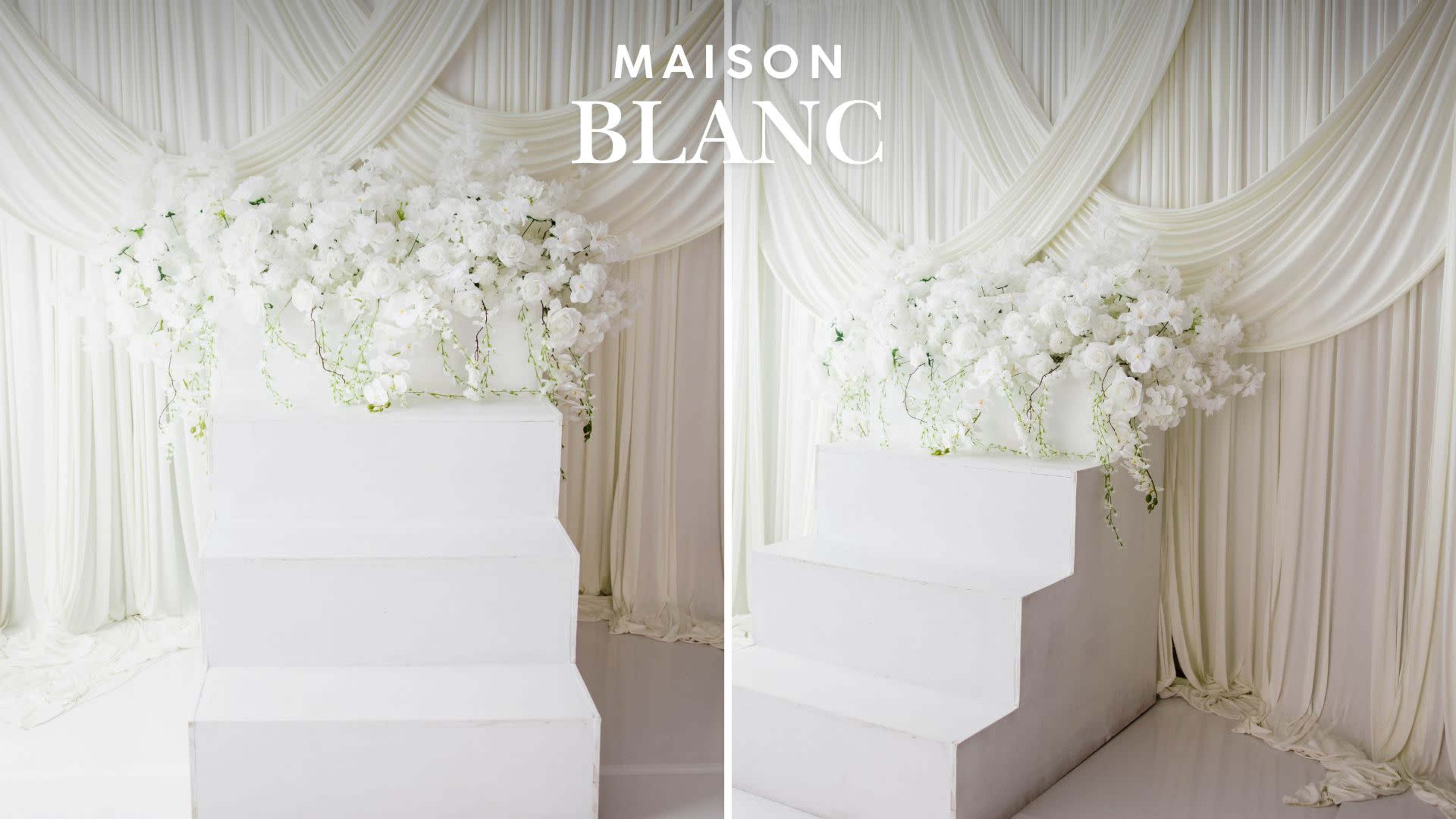 A white staircase is adorned with a floral arrangement of white orchids against a backdrop of draped white fabric.