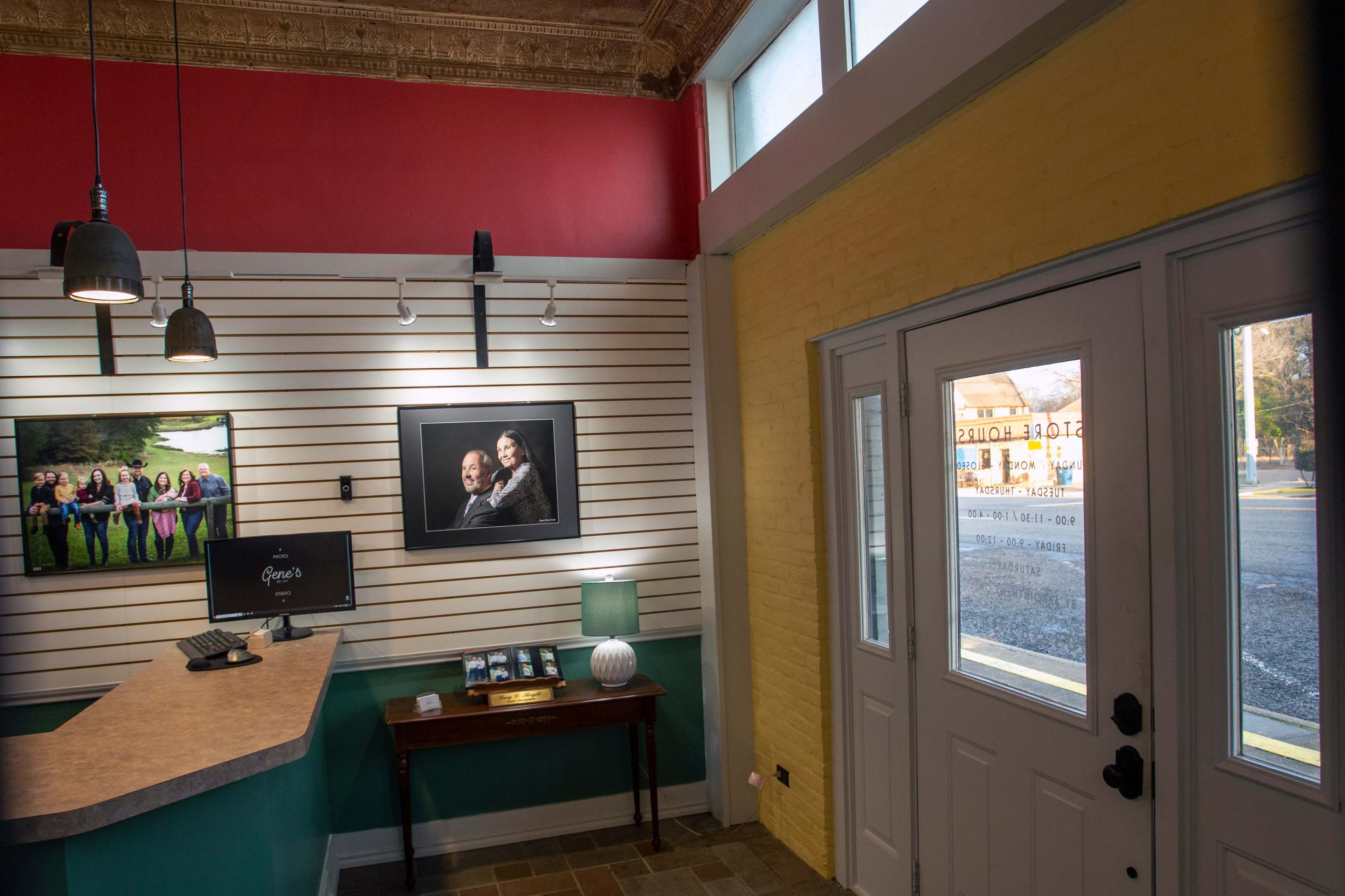 The interior of a reception area features a front desk with a computer, art displays on the walls, and large windows allowing natural light to enter.