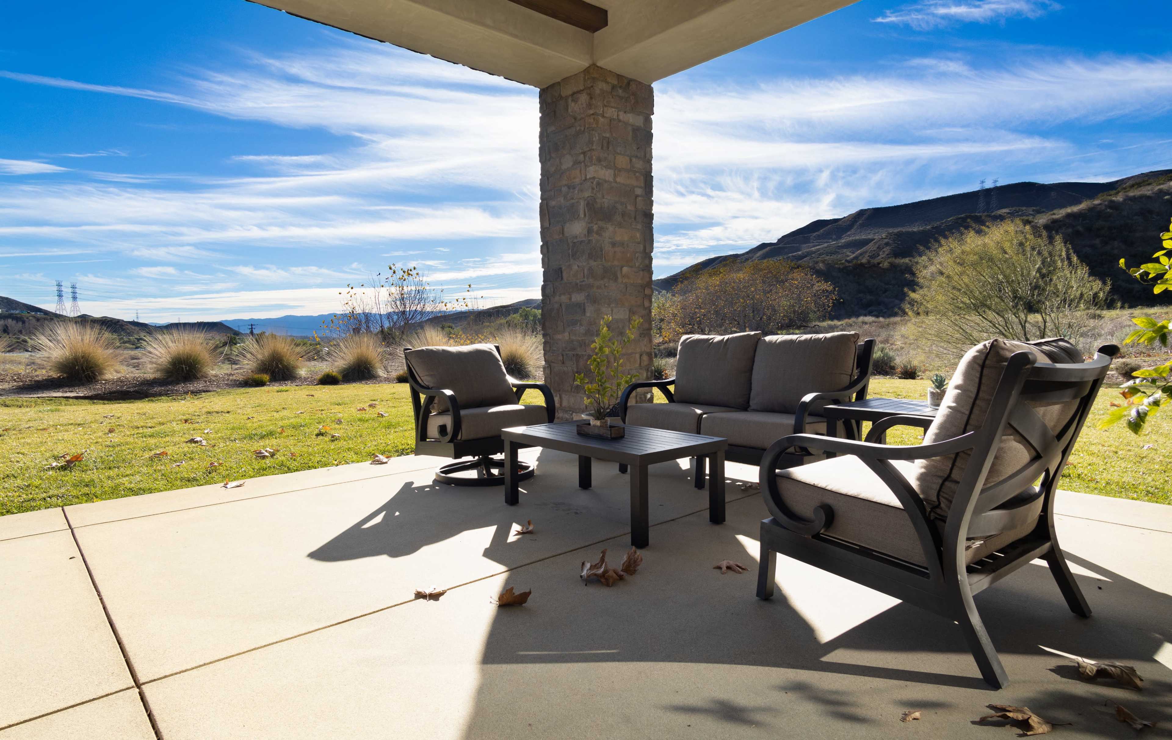A patio area features a table and four chairs with a view of mountains and blue skies in the background.
