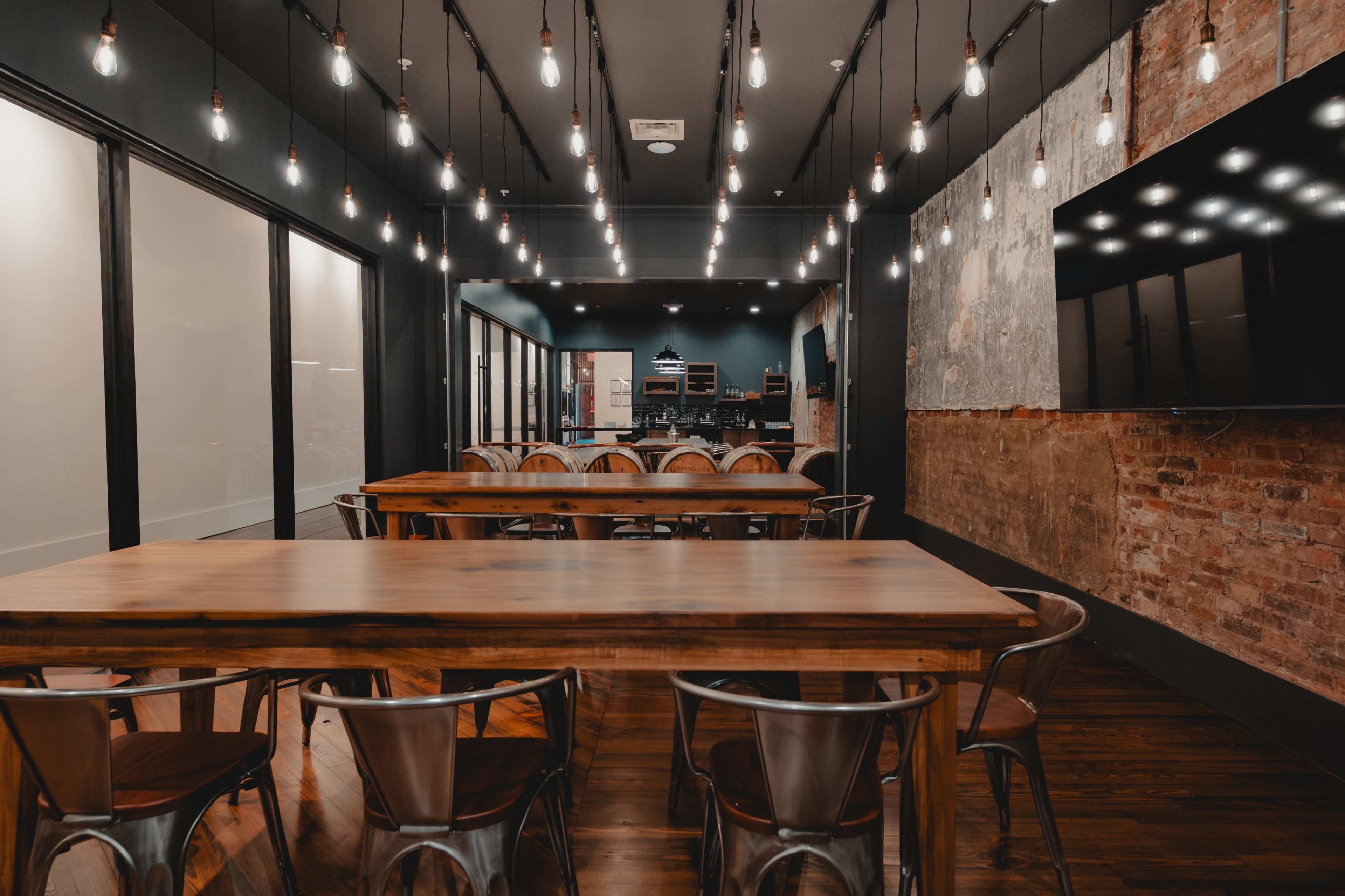 A modern conference room features a long wooden table surrounded by metal chairs, illuminated by hanging light bulbs.