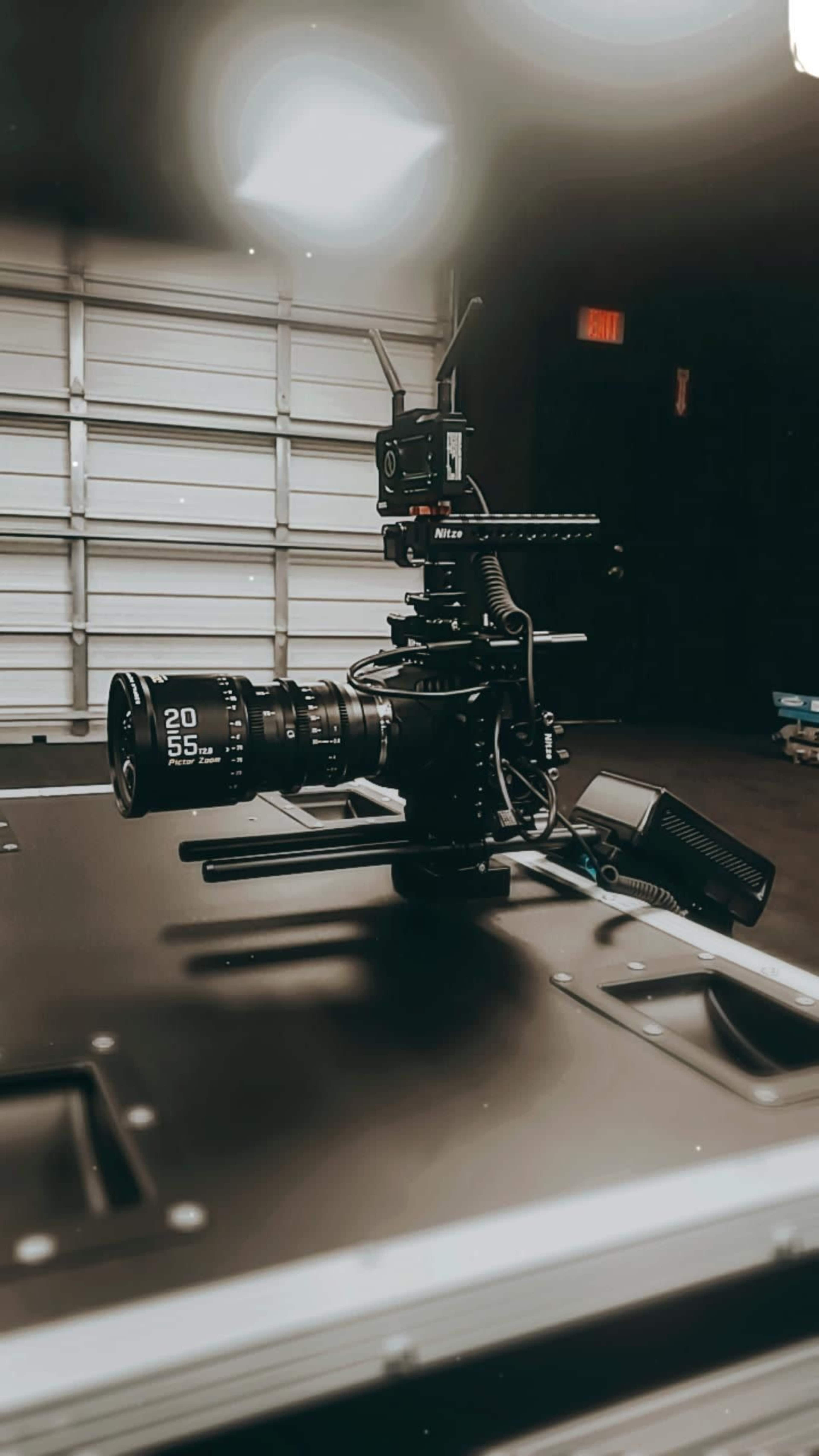 A camera setup with a zoom lens and wireless transmitter is placed on a black tabletop in a garage.