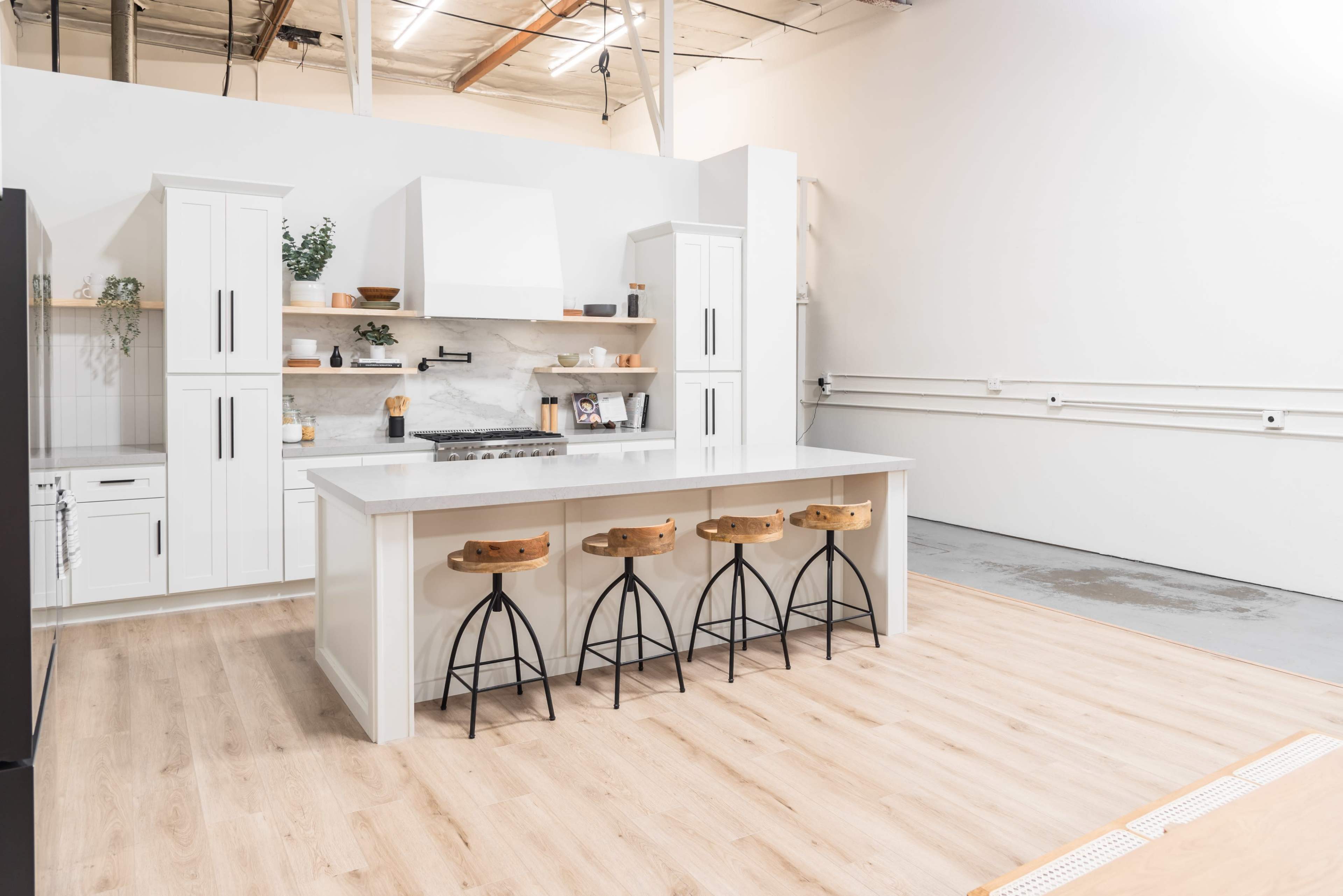 A modern kitchen with white cabinetry, a central island featuring four bar stools, and a minimalist design aesthetic.