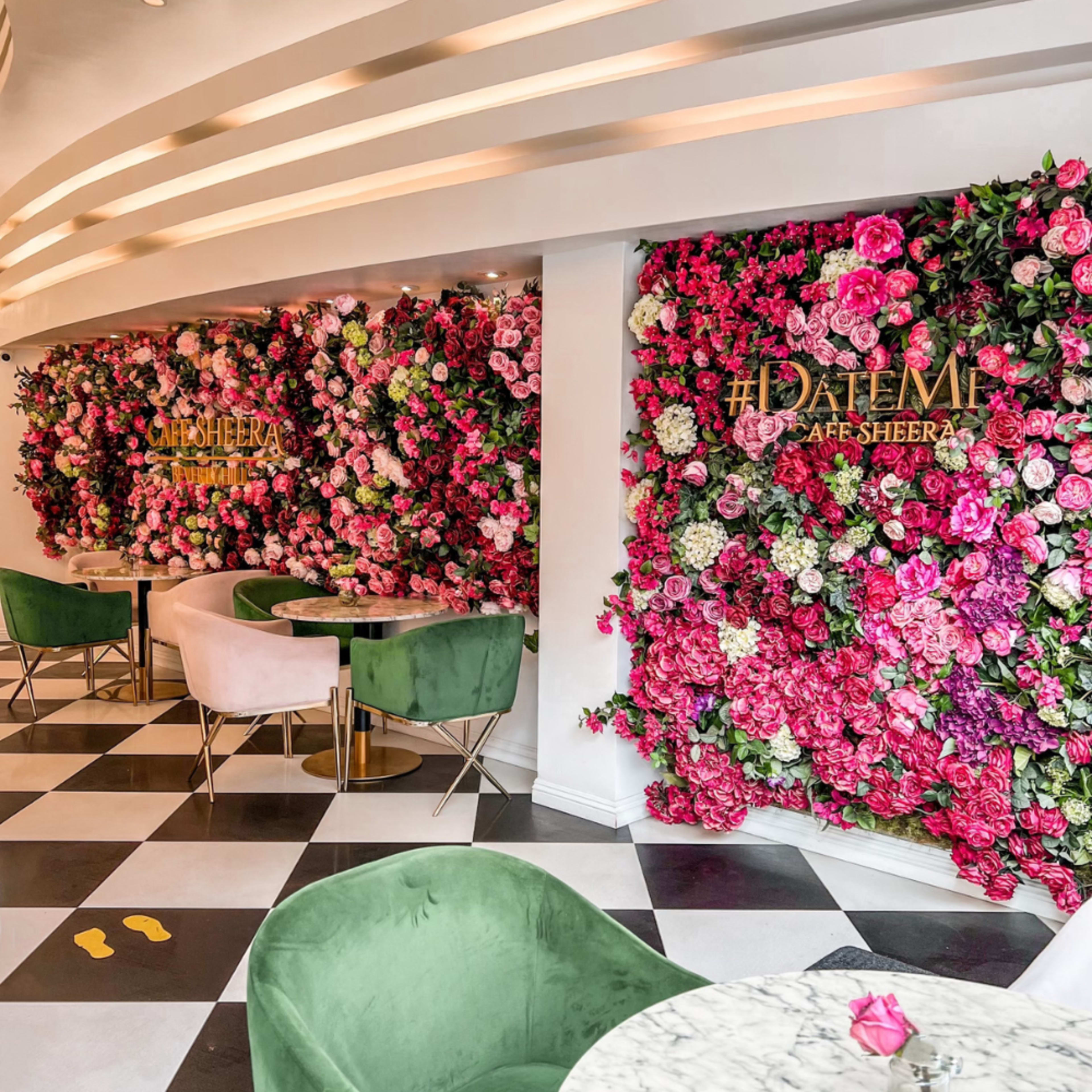 A café interior with floral wall decorations, two round tables, and plush seating in green and pink.