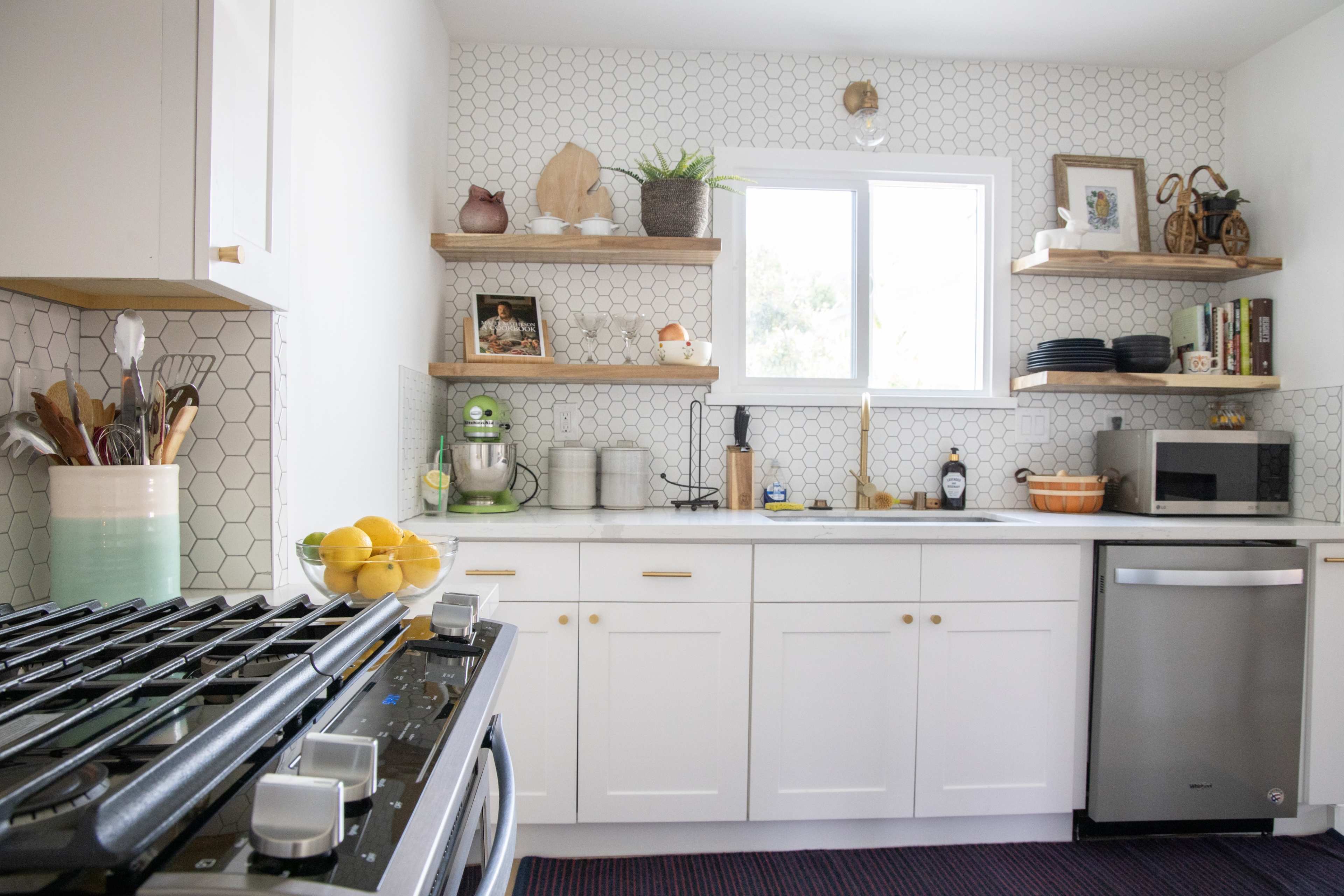 A modern kitchen features white cabinetry, a stainless steel dishwasher, and open shelves displaying various kitchen items and decor.