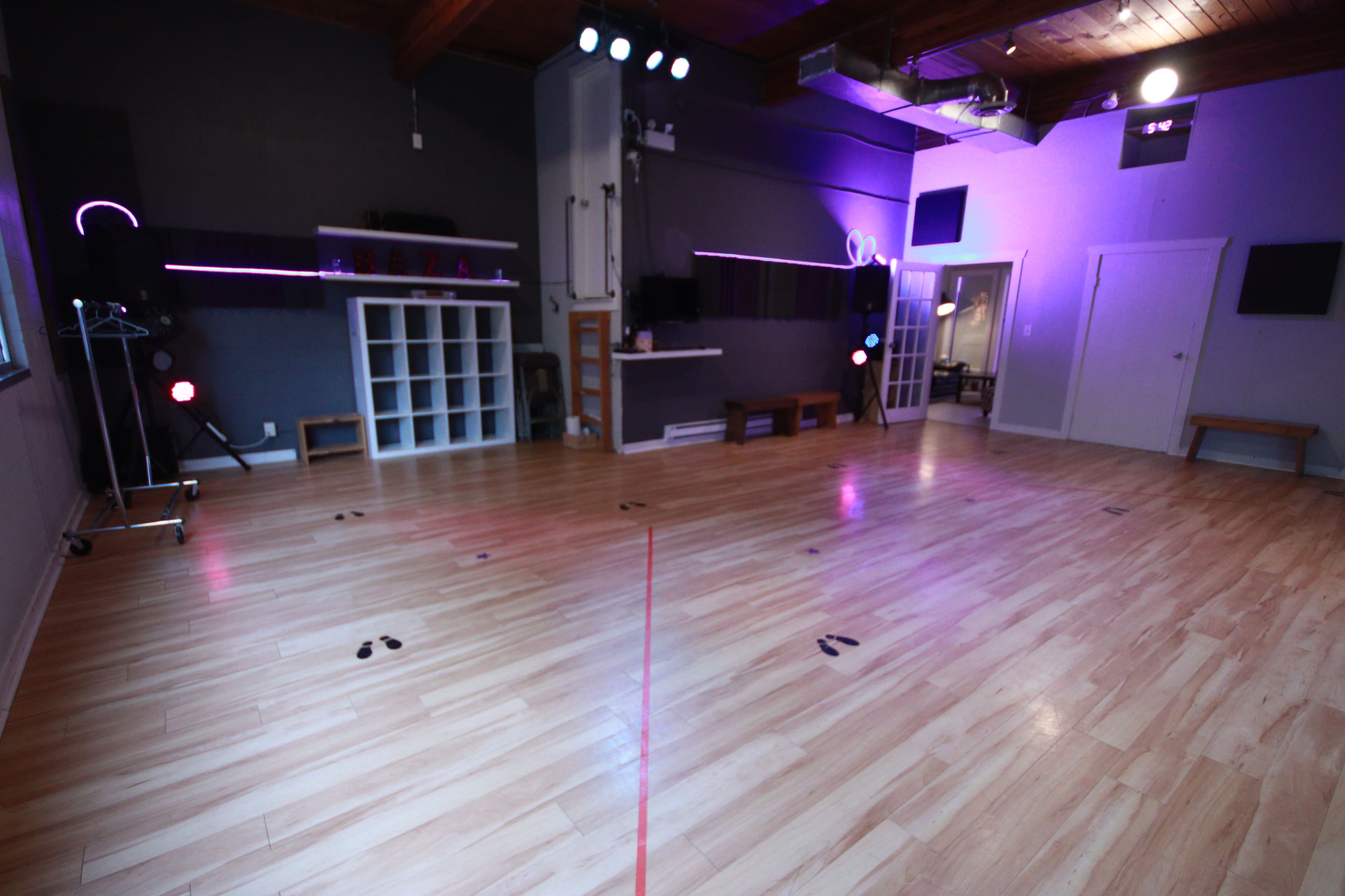 A spacious dance studio with a wooden floor, ambient lighting, and a mirrored wall.