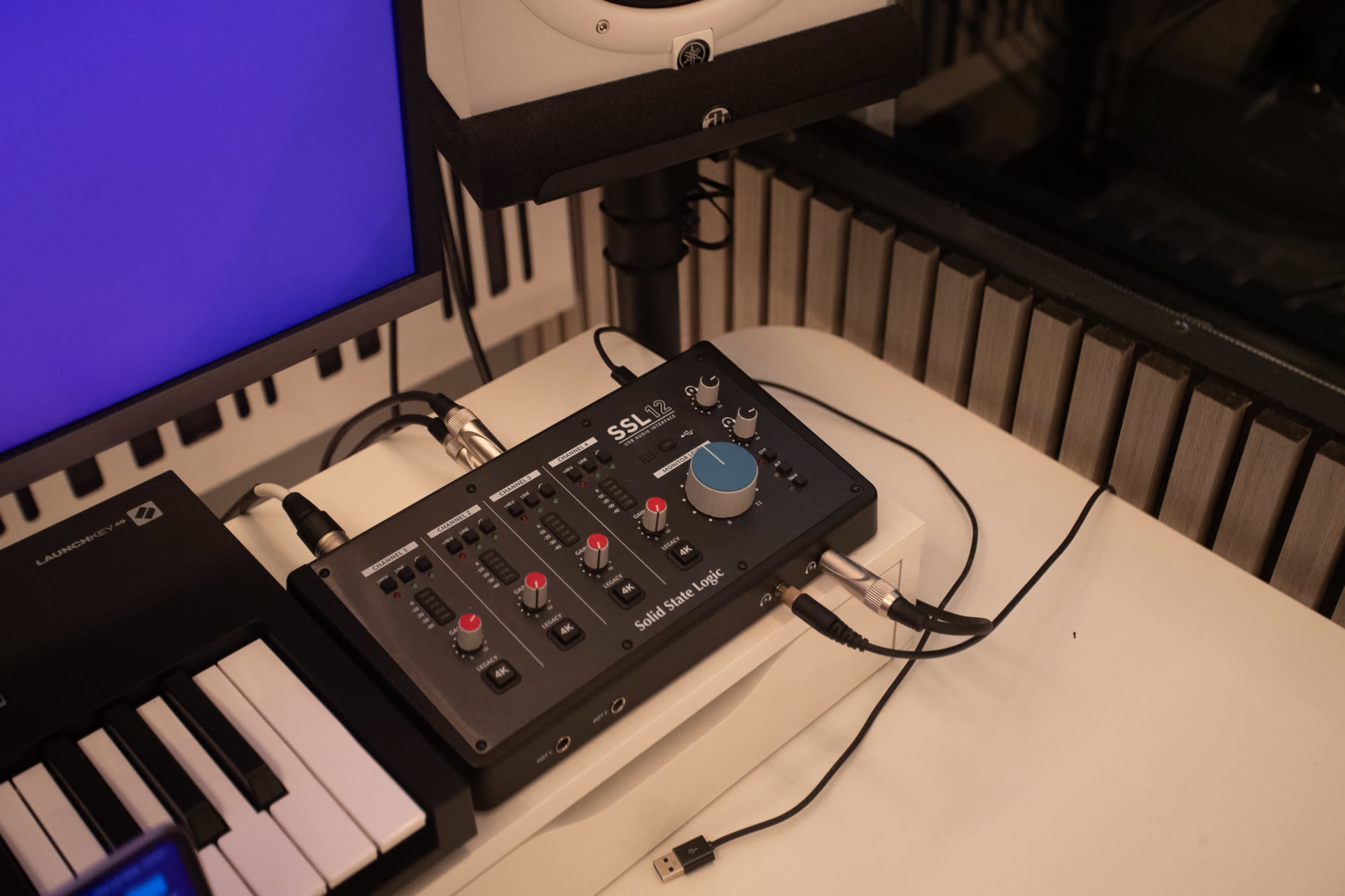 A solid-state audio interface is positioned on a desk next to a keyboard and a monitor in a recording studio.