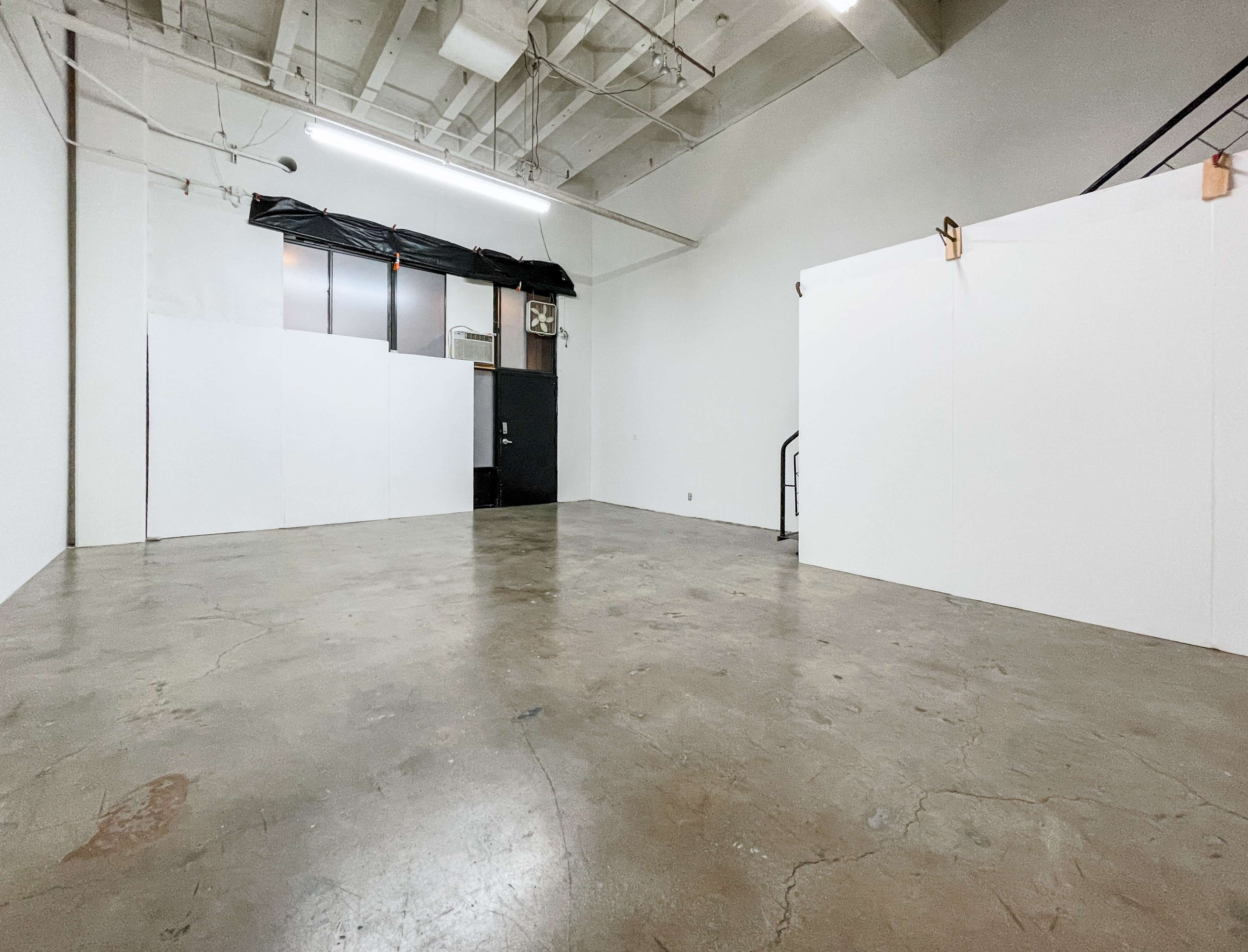 The room features bare concrete flooring and white walls with a dark door and minimal furnishings.