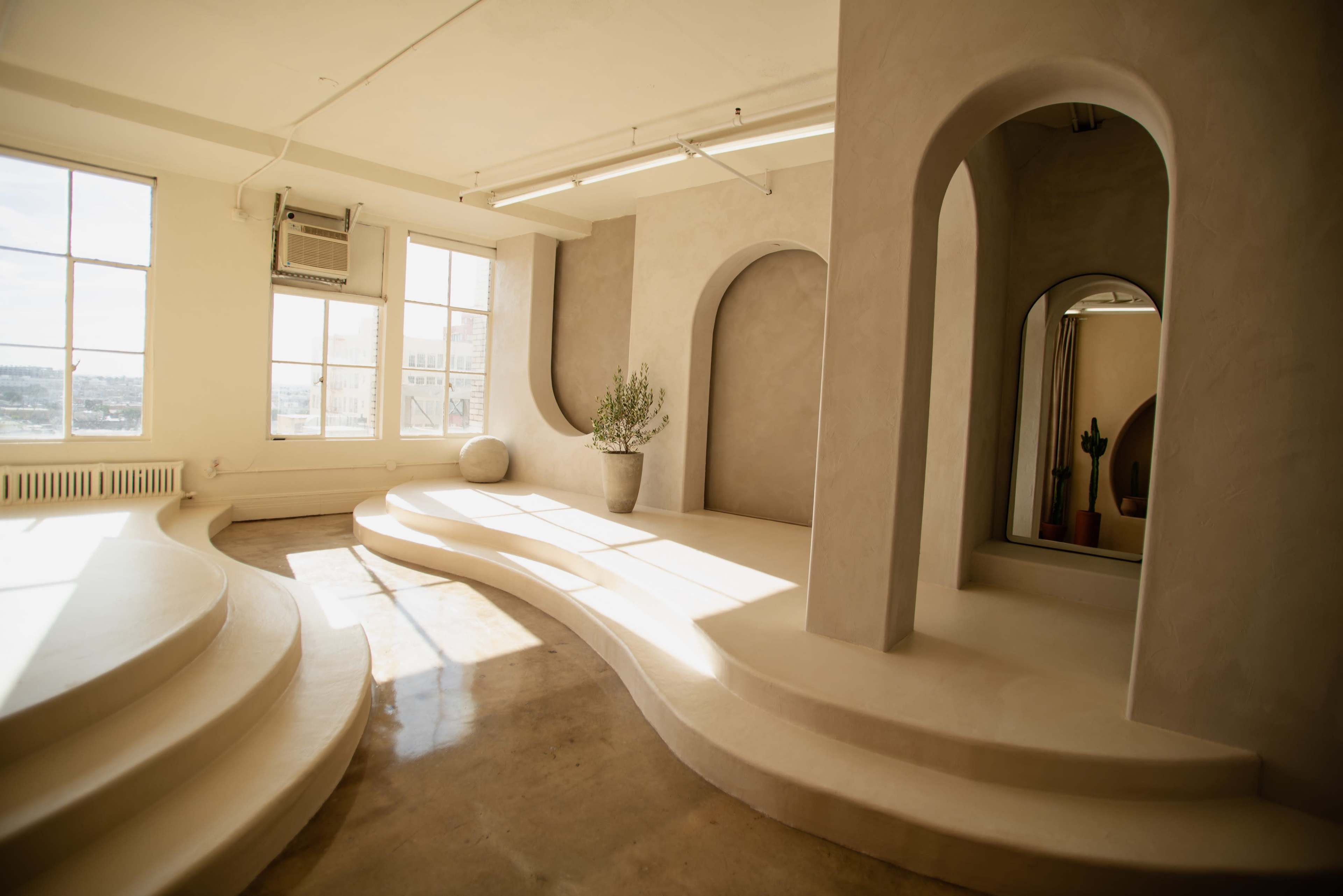 A spacious room features smooth, curved platforms and arches, with large windows allowing natural light to fill the space.