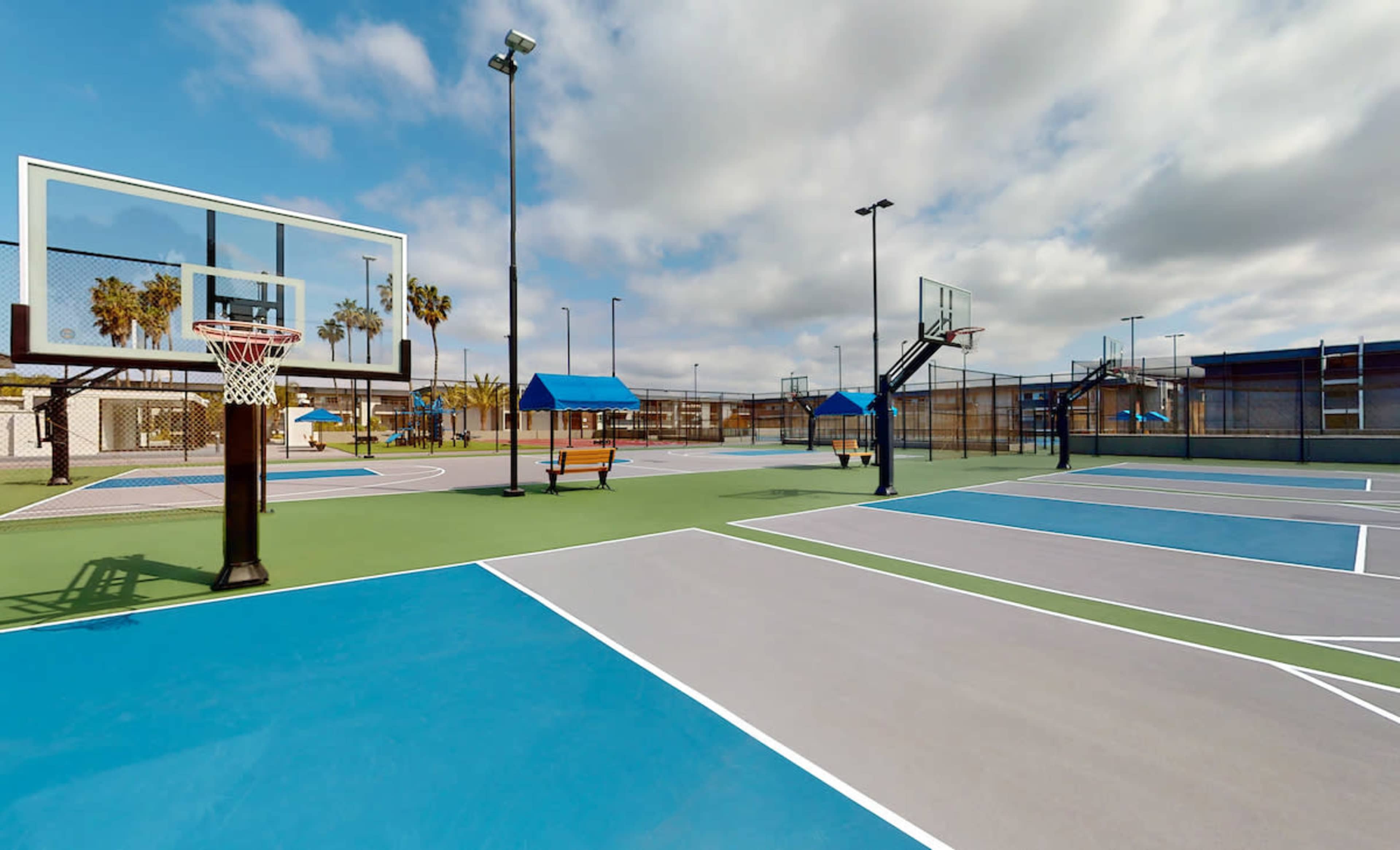 A brightly lit outdoor basketball court with multiple hoops and colorful surface markings.