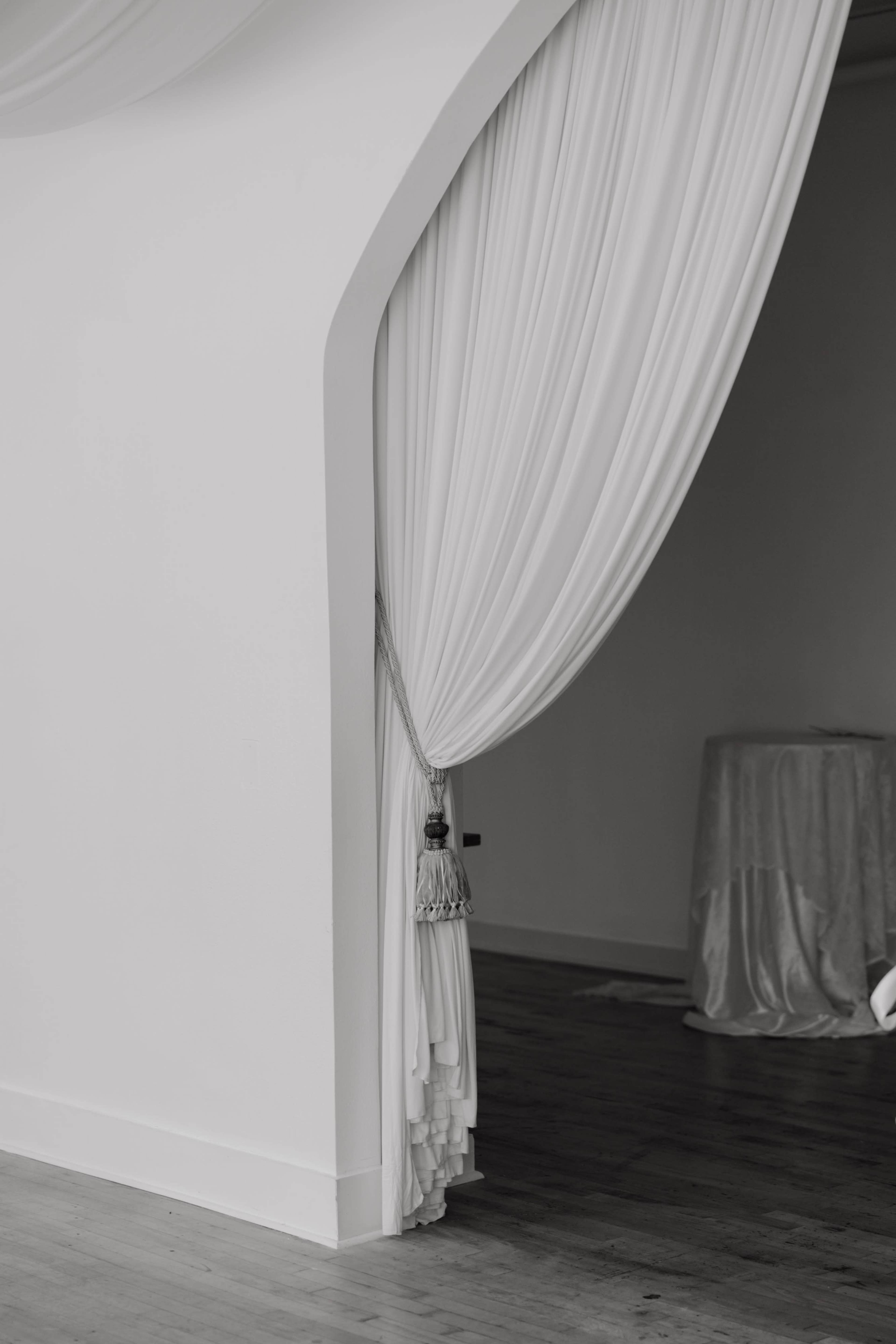 A white curtain drapes elegantly over an arched entrance, partially revealing a room with soft furnishings.