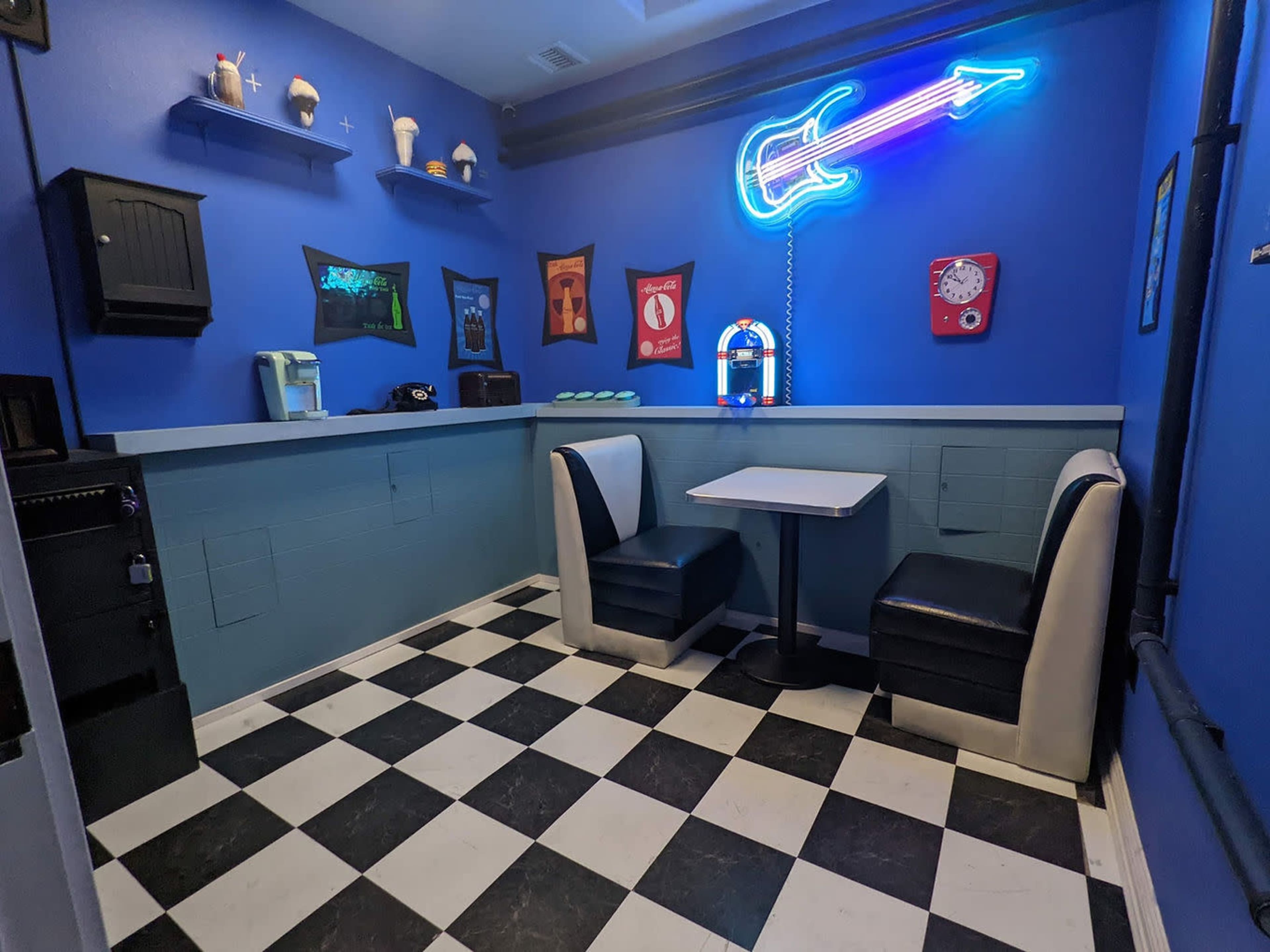A small diner-like room with blue walls, a checkered floor, and a table with two retro-style chairs.