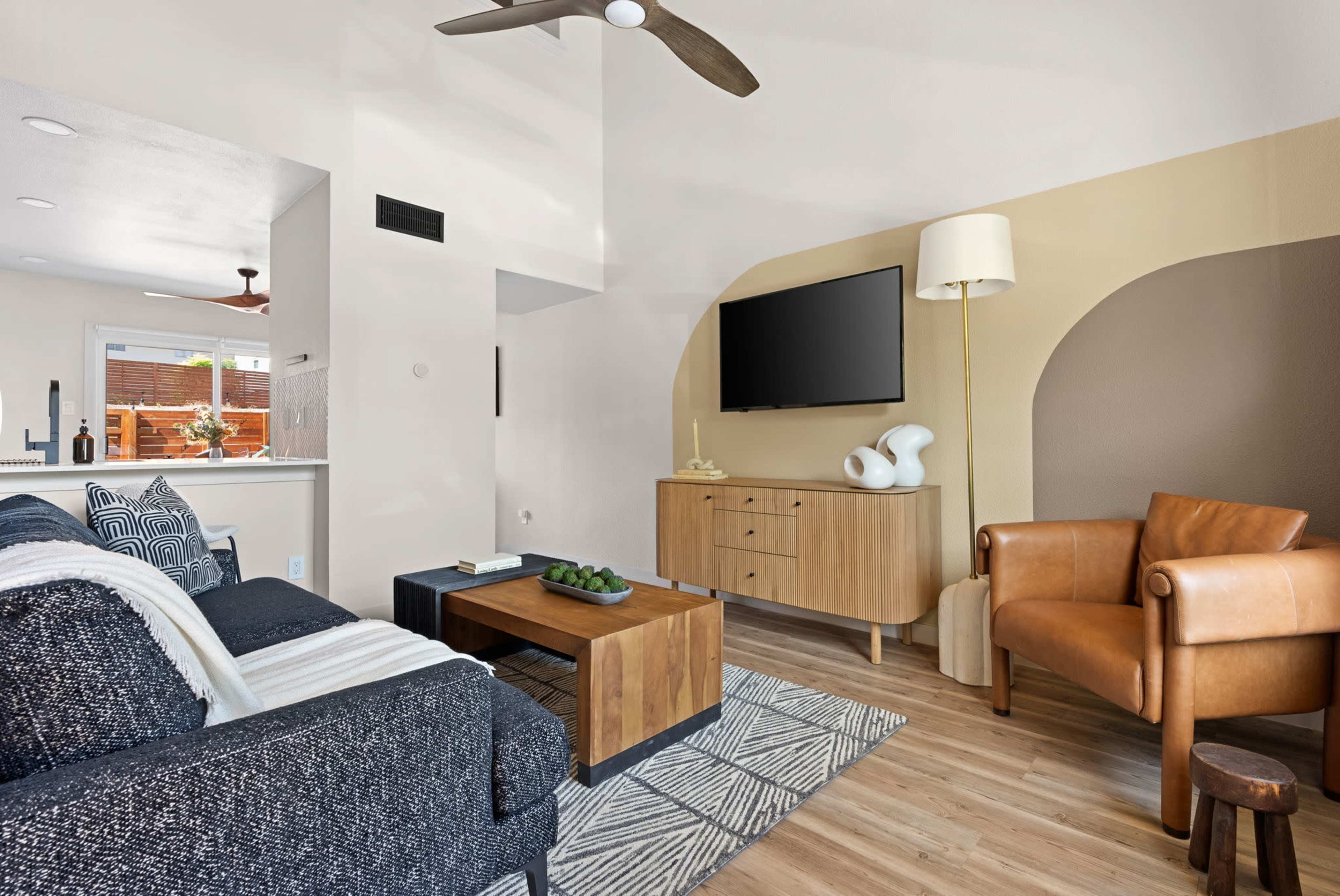 The living room features a sofa, a wooden entertainment center with a television, a leather armchair, and a coffee table with decorative items.