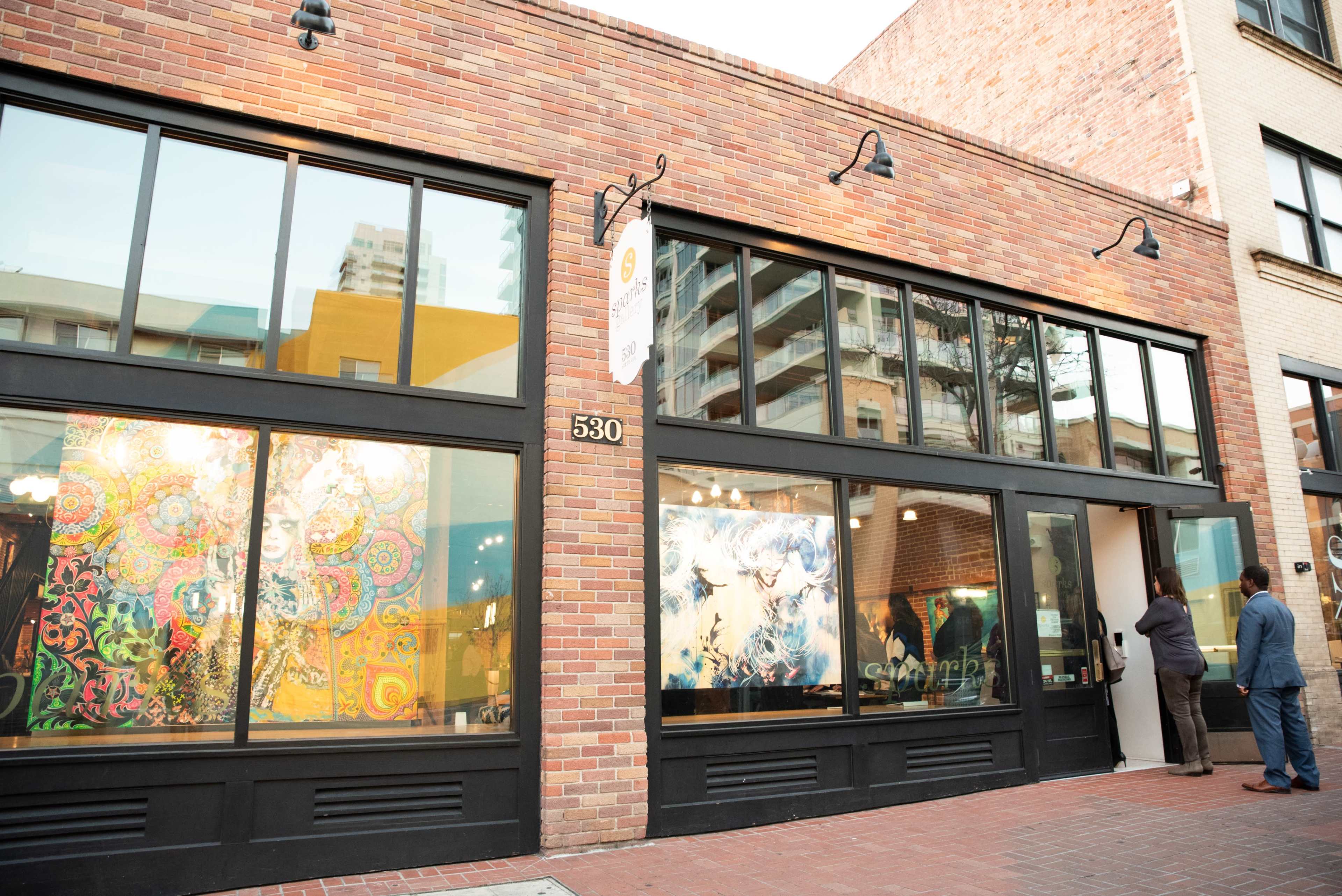A brick building with large windows displaying colorful artwork, and a person entering through the door.